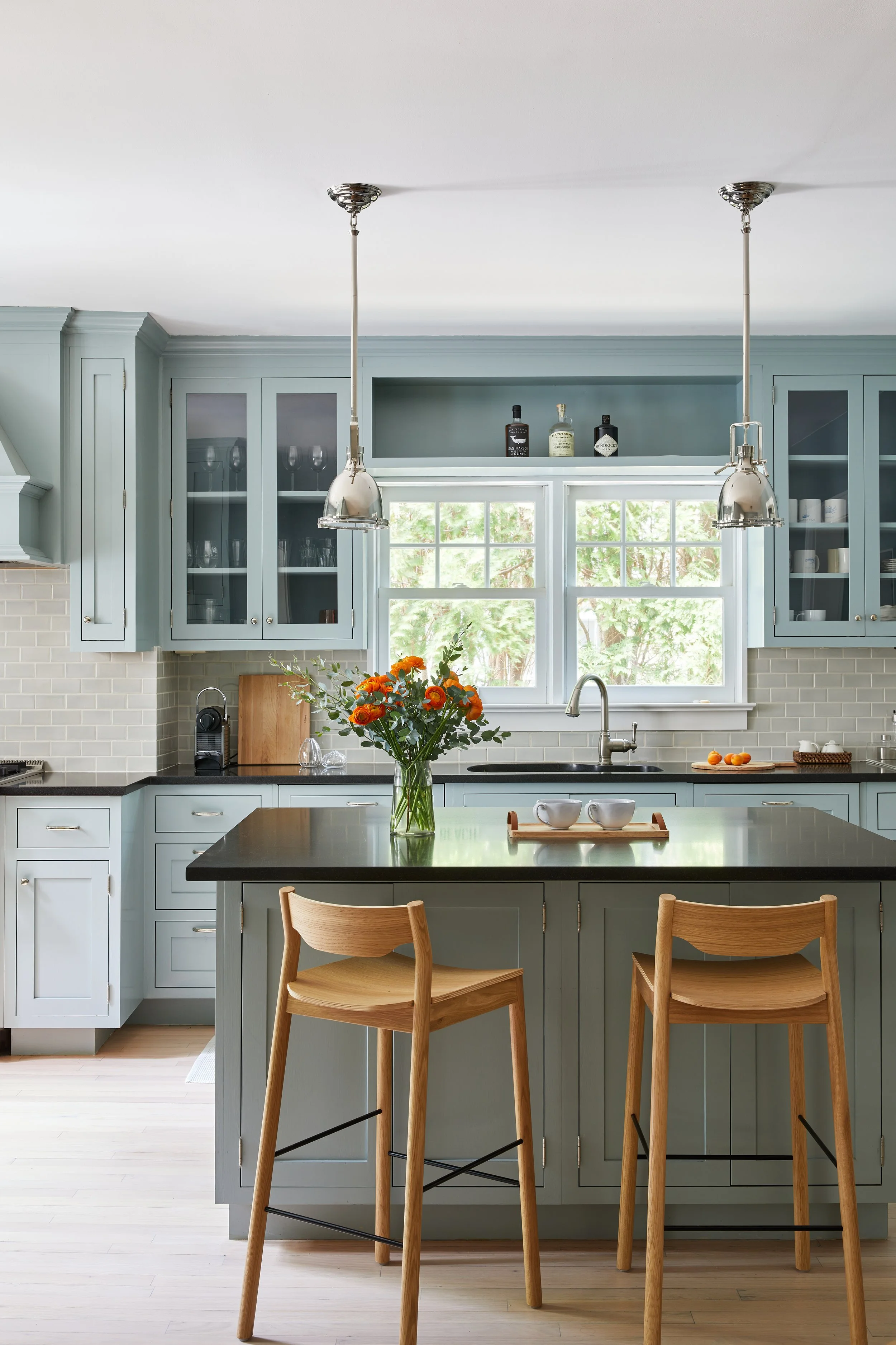 Coastal Hamptons kitchen by Southampton NY interior designer with duck-egg blue cabinetry, black countertops and oak bar stools