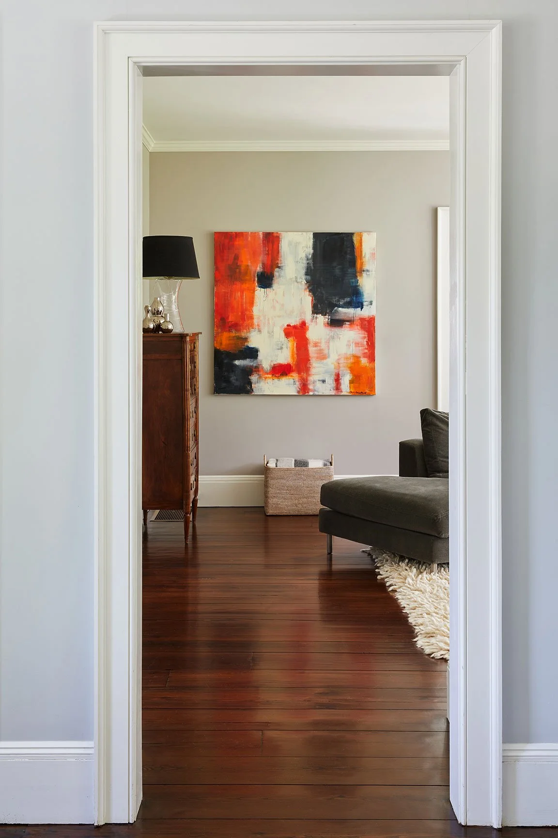 Nearby Darien CT living room with bold red and navy abstract canvas, antique wood chest, black-shaded lamp, dark green chaise and mahogany floors