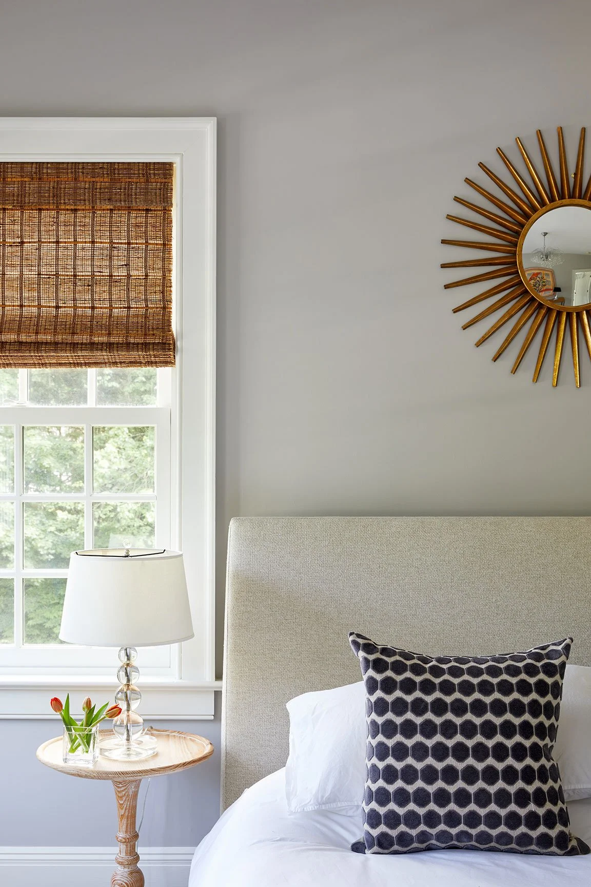 Bedroom detail with linen headboard, geometric pillow, woven roman shades, and glass bedside lamp in a Darien CT home renovation by Ginger Lemon Indigo