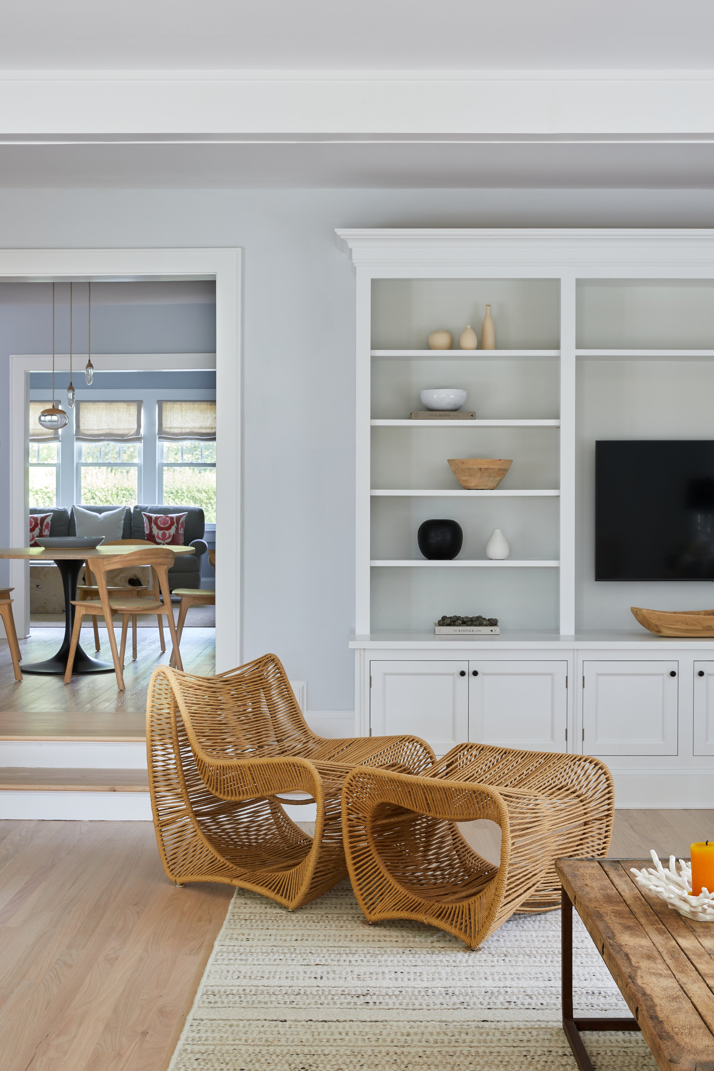 Coastal Hamptons living room by Southampton NY interior designer with sculptural rattan lounge chairs, white built-in shelving and pale oak floors