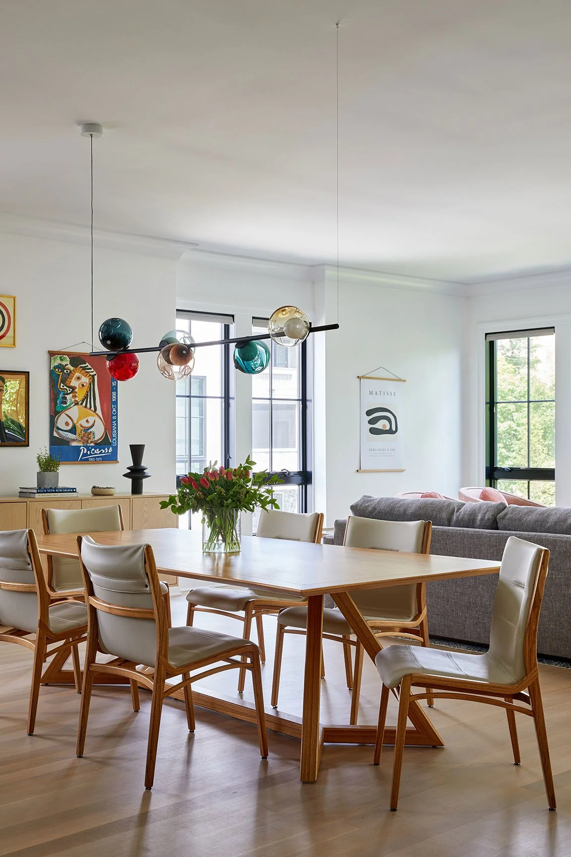 Open plan dining area with Sossego ZYV table, Lily chairs, multicolored handblown glass pendant, Picasso poster, and grey sectional in a Rye NY condo by Ginger Lemon Indigo