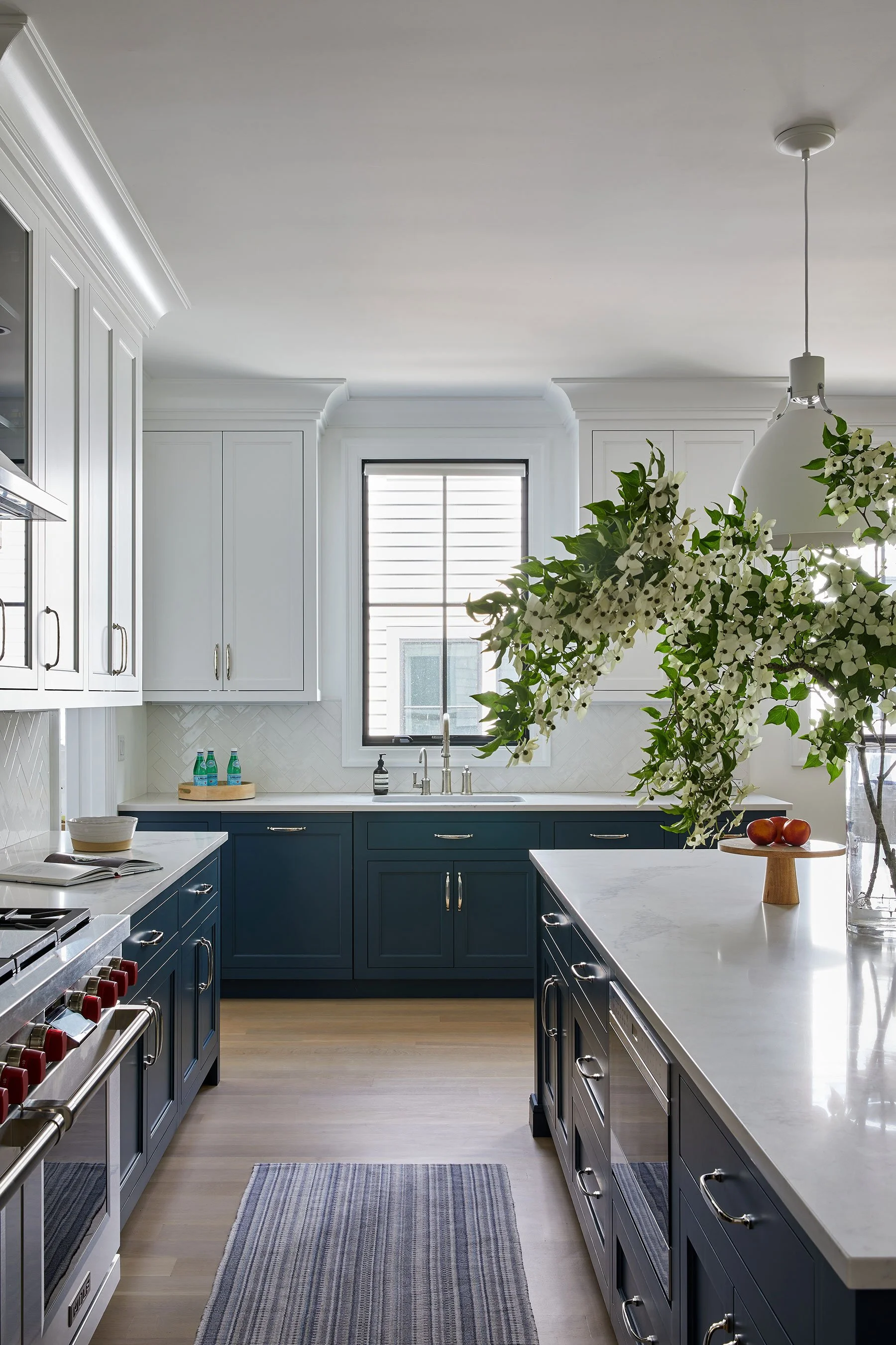 Two tone kitchen with navy lower cabinets, white upper cabinets, herringbone tile backsplash, and dome pendant lights in a Rye NY condo by Ginger Lemon Indigo