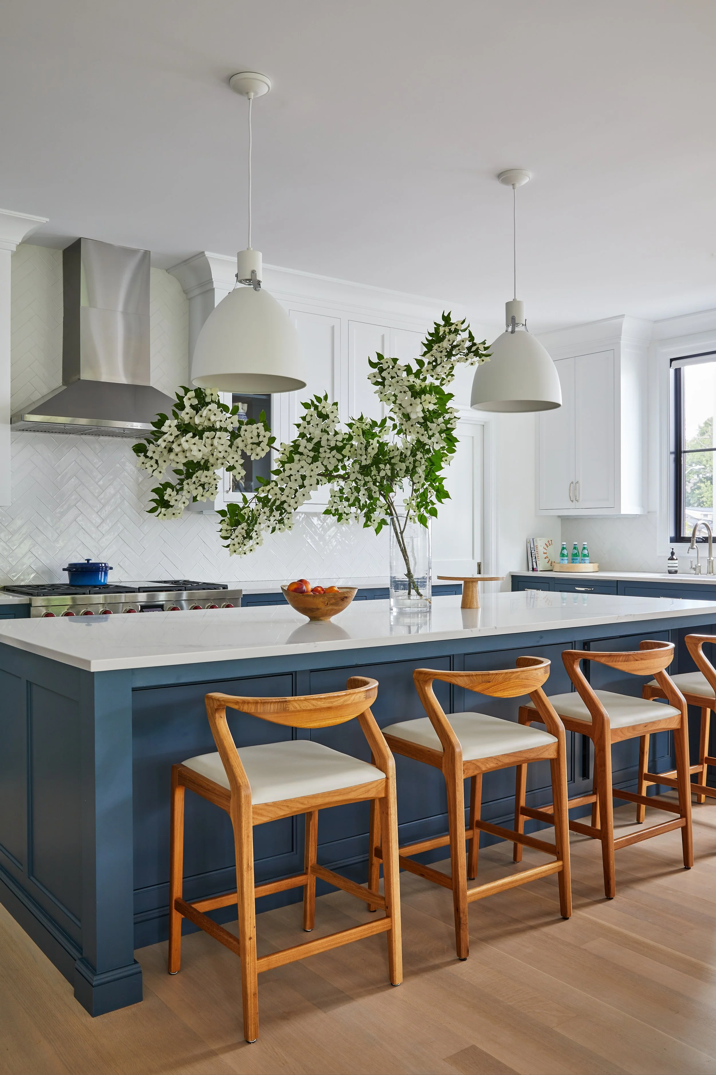 Full service kitchen design with custom navy cabinetry, white quartz island, herringbone tile backsplash, and natural wood bar stools by Ginger Lemon Indigo, Connecticut