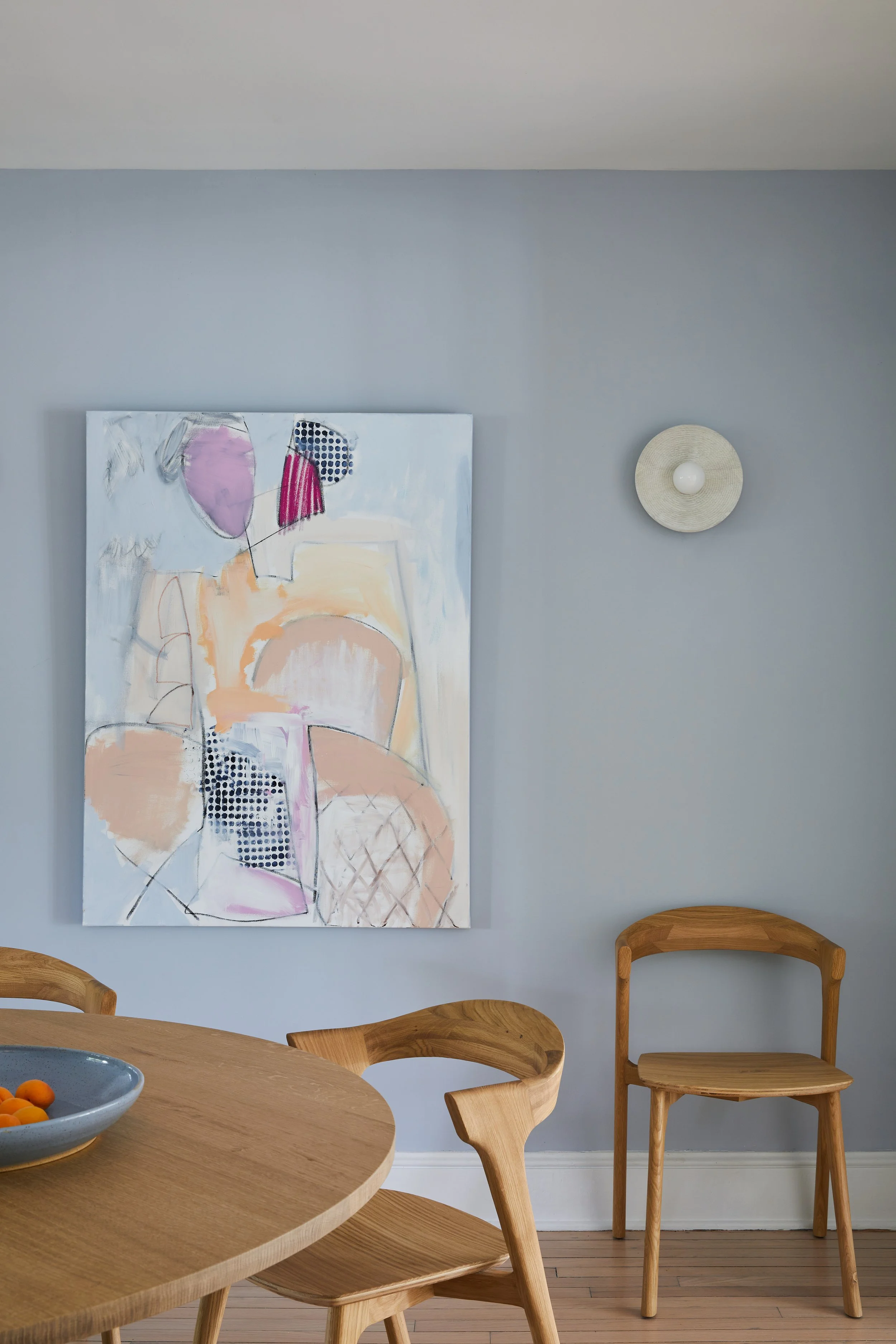 Coastal Hamptons dining nook by Southampton NY interior designer with soft blue walls, an abstract canvas by Allison Meyler, oak dining chairs and a round oak table