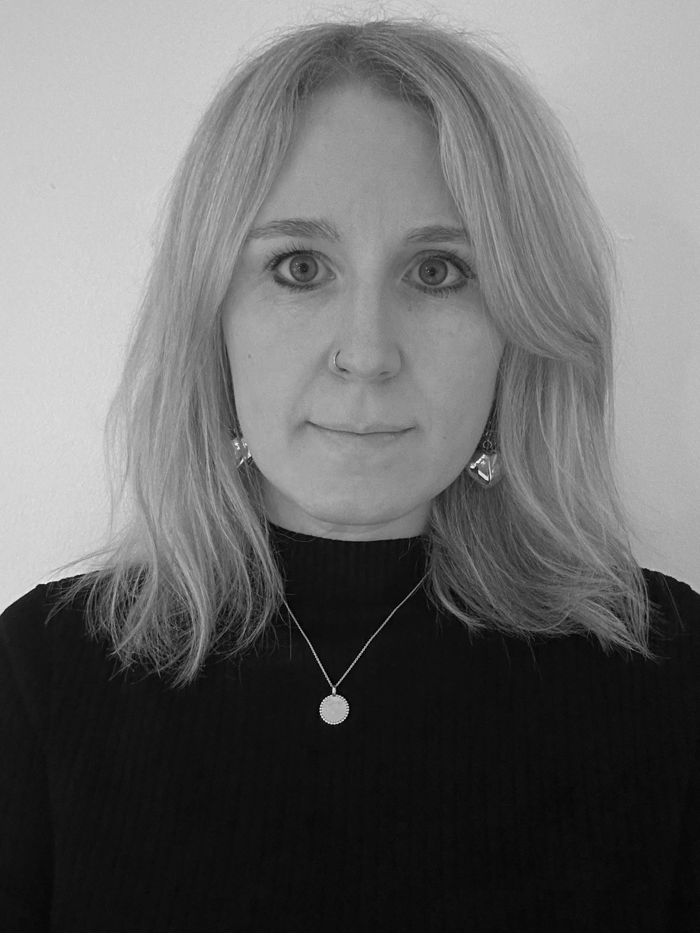 Black and white portrait of a person with long hair wearing a black top and necklace.