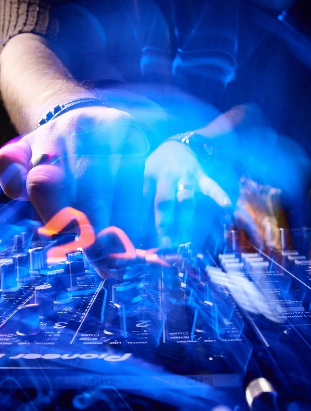 A DJ is adjusting controls on a glowing sound mixer with blue and purple lights.
