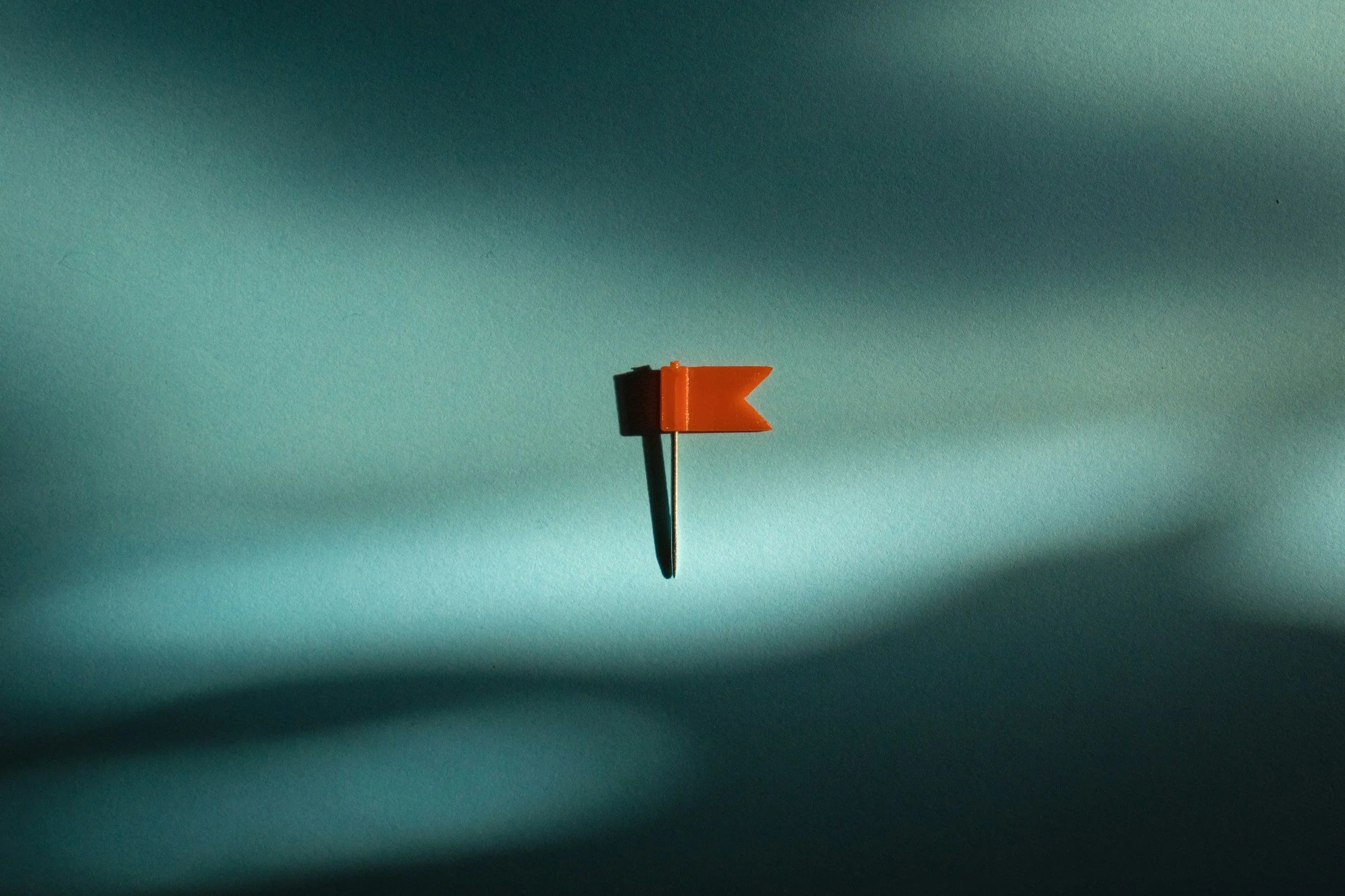 A small orange arrow-shaped object on a thin metal stick against a textured teal background.