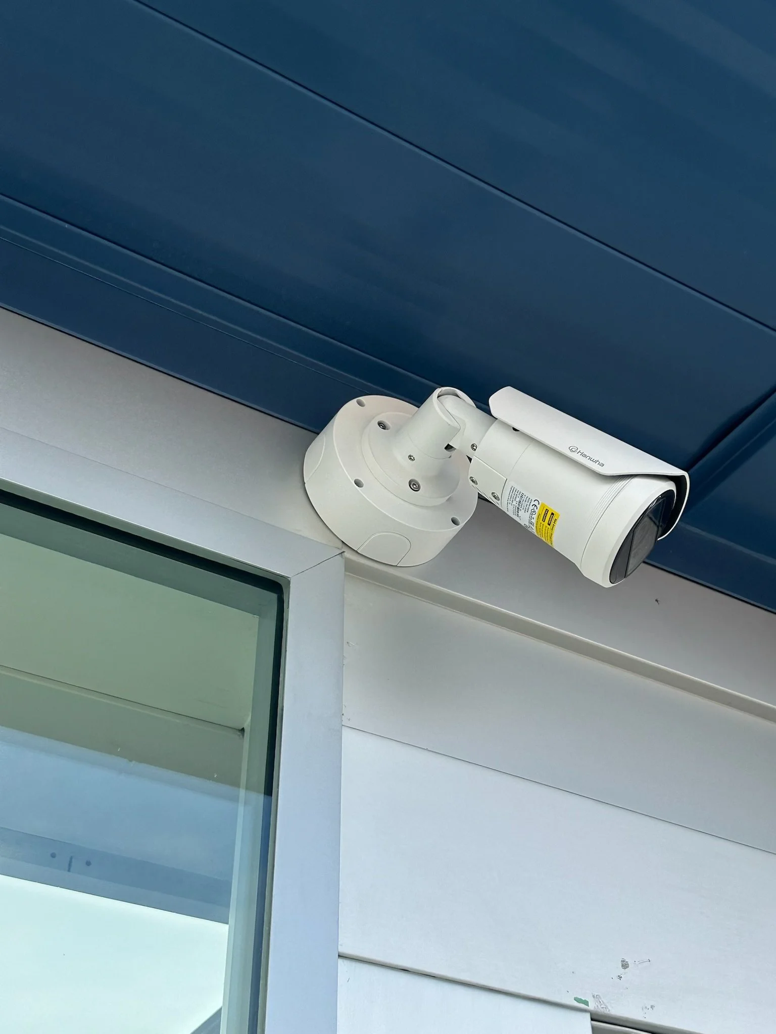 Security camera mounted on a flat surface beneath a blue panel ceiling.