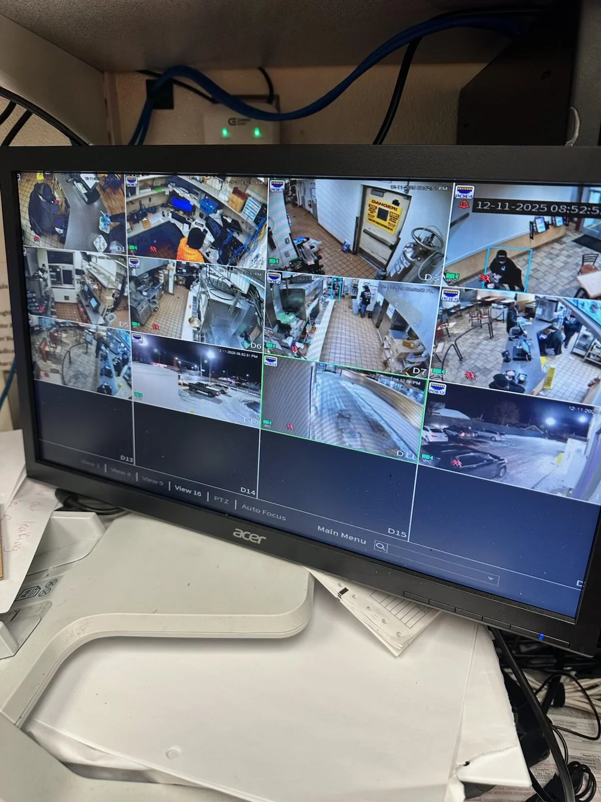 Video surveillance monitor showing multiple camera feeds of a parking lot, store interior, and outdoor scenes at night, with timestamp and various security icons.