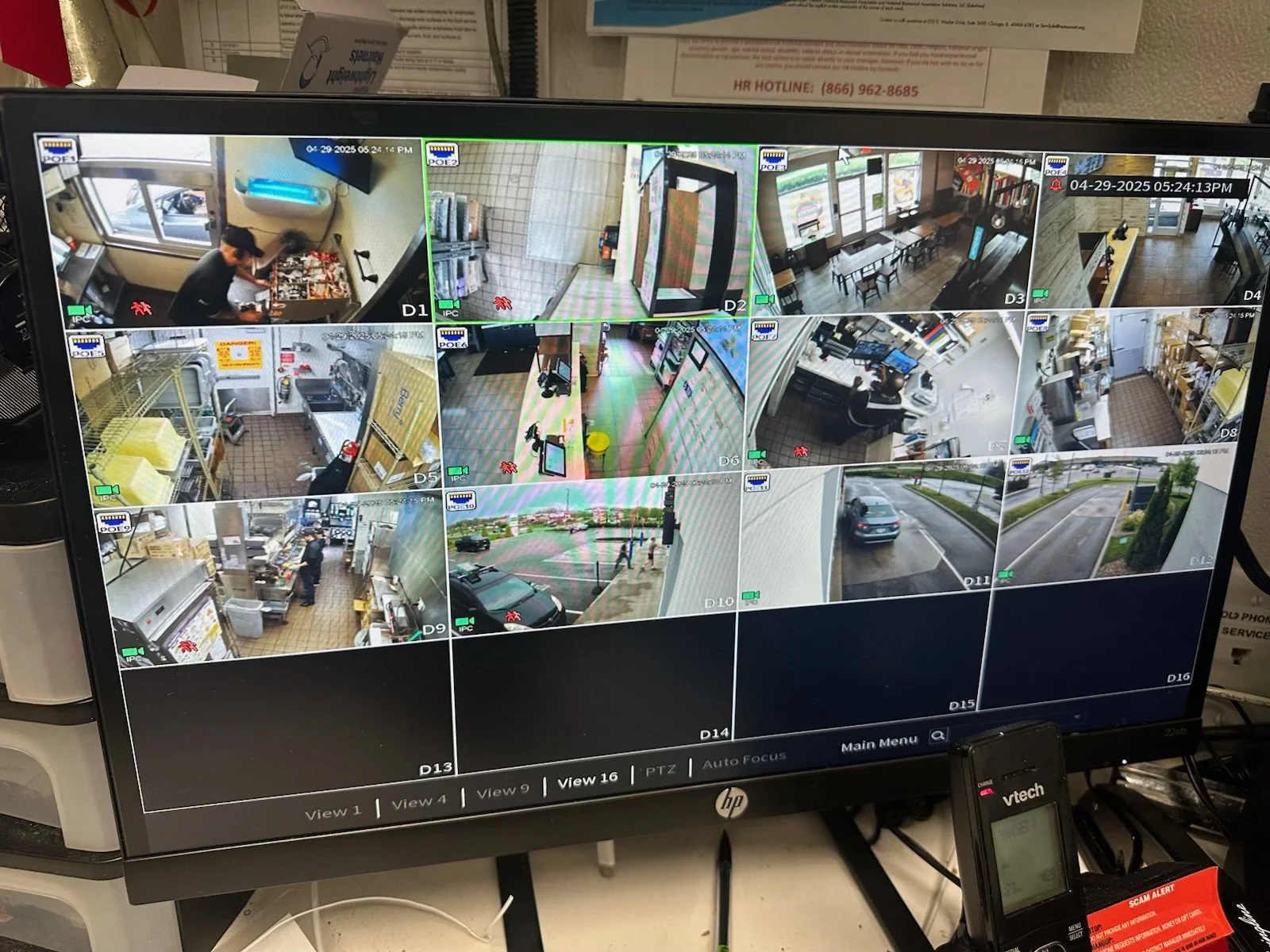 A computer monitor showing multiple surveillance camera feeds of indoor and outdoor areas of a restaurant or store, including kitchen, office, parking lot, and streets.