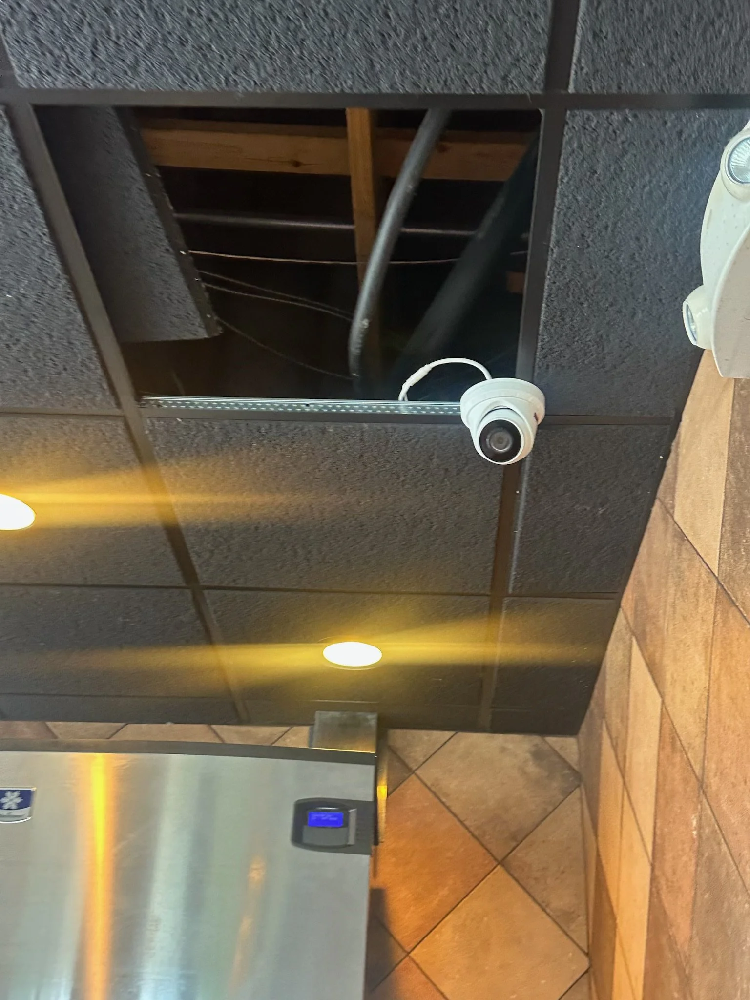 A security camera mounted on a wall with brown tiles in the background.