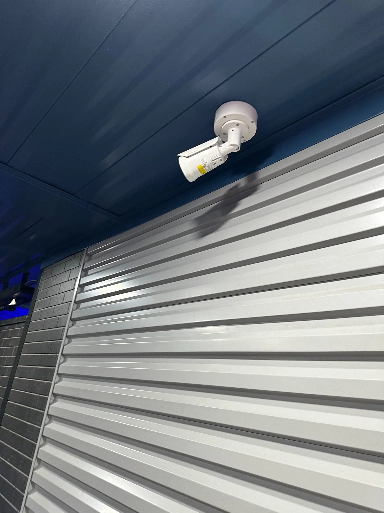Security camera mounted on a blue ceiling next to a white garage door.