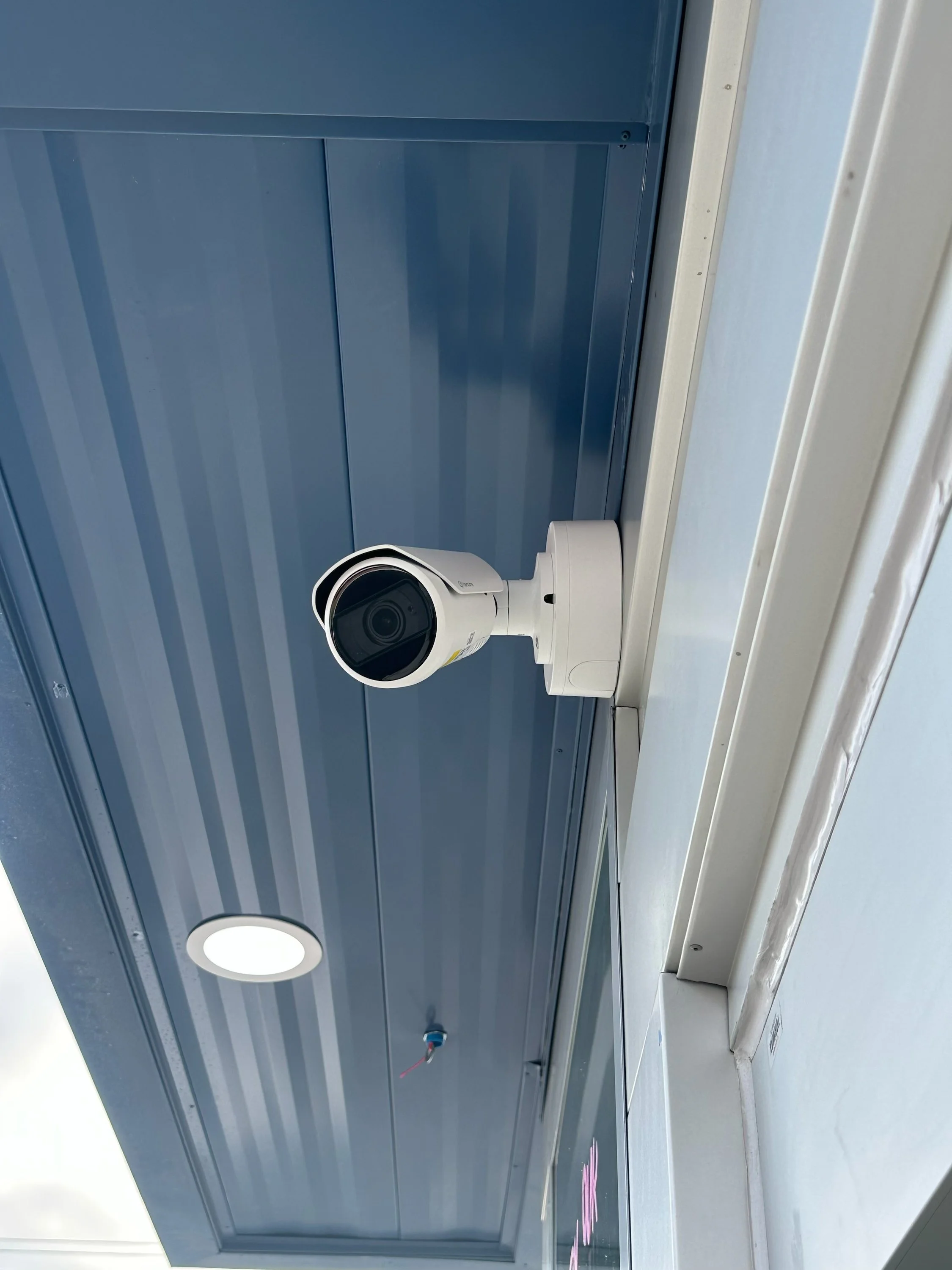 Security camera mounted on a blue wall near a white door frame.
