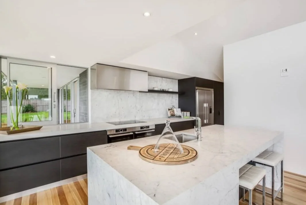 Modern kitchen renovation with white marble island, stainless steel appliances & dark lower cabinets.