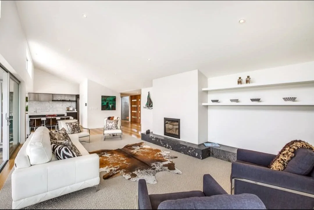 Modern living room with raking ceiling, fireplace, open modern kitchen, and sliding glass doors.