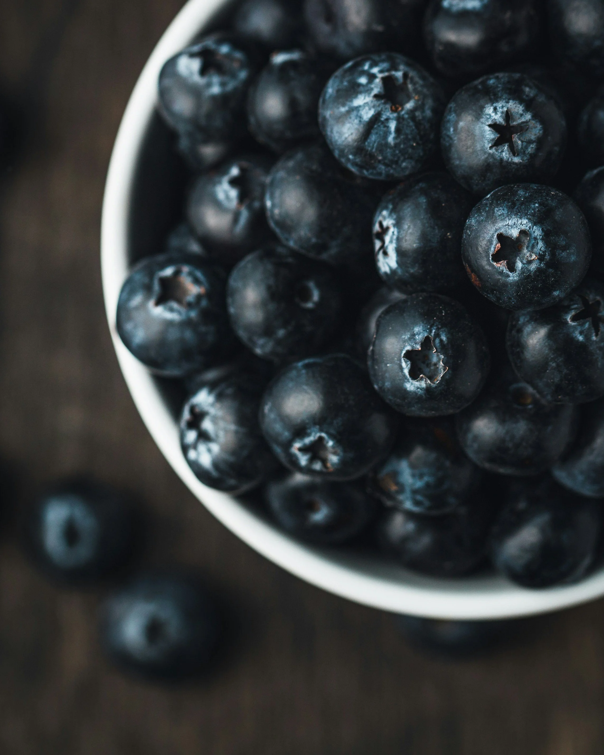 Close-up of fresh blueberries in a white bowl with a dark background.