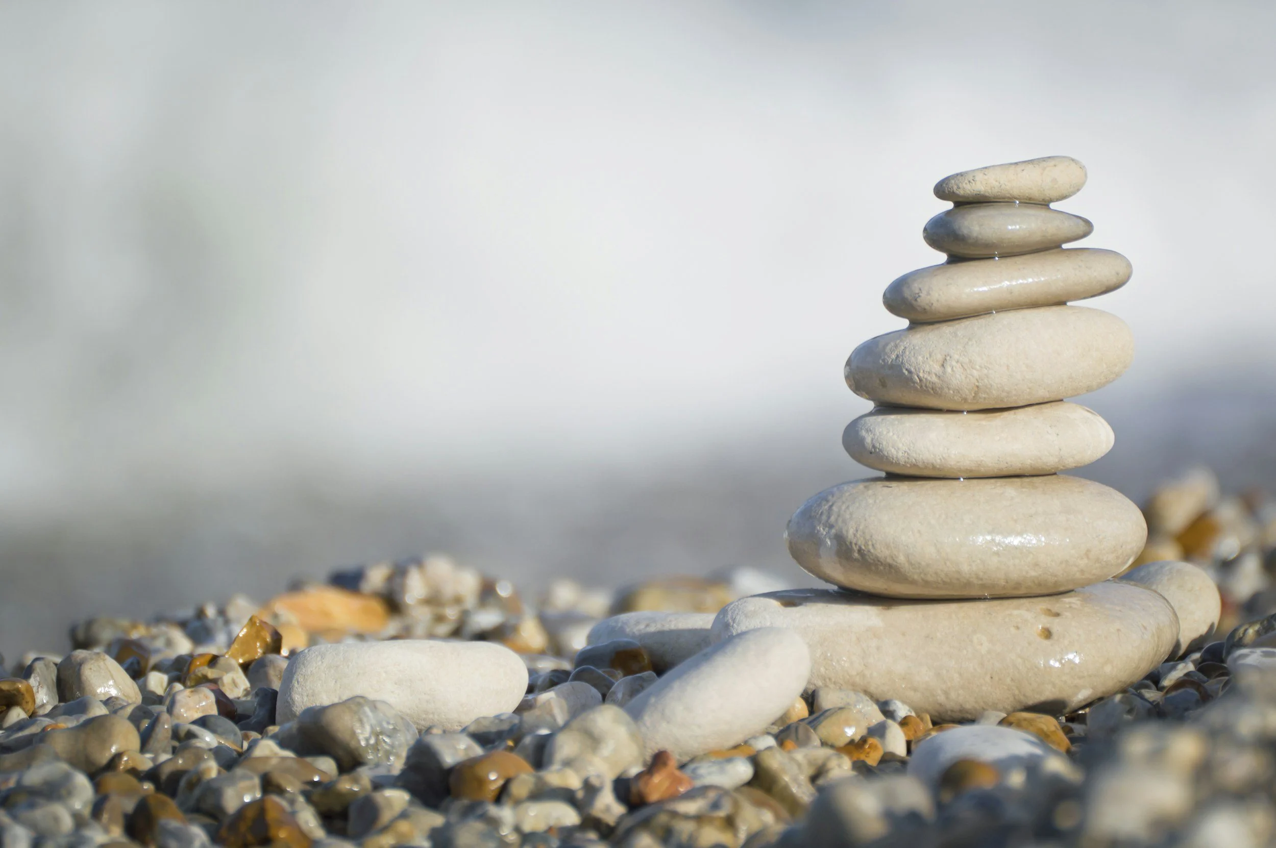 Stack of smooth, rounded stones balanced on a pebble-covered surface with a cloudy sky background.