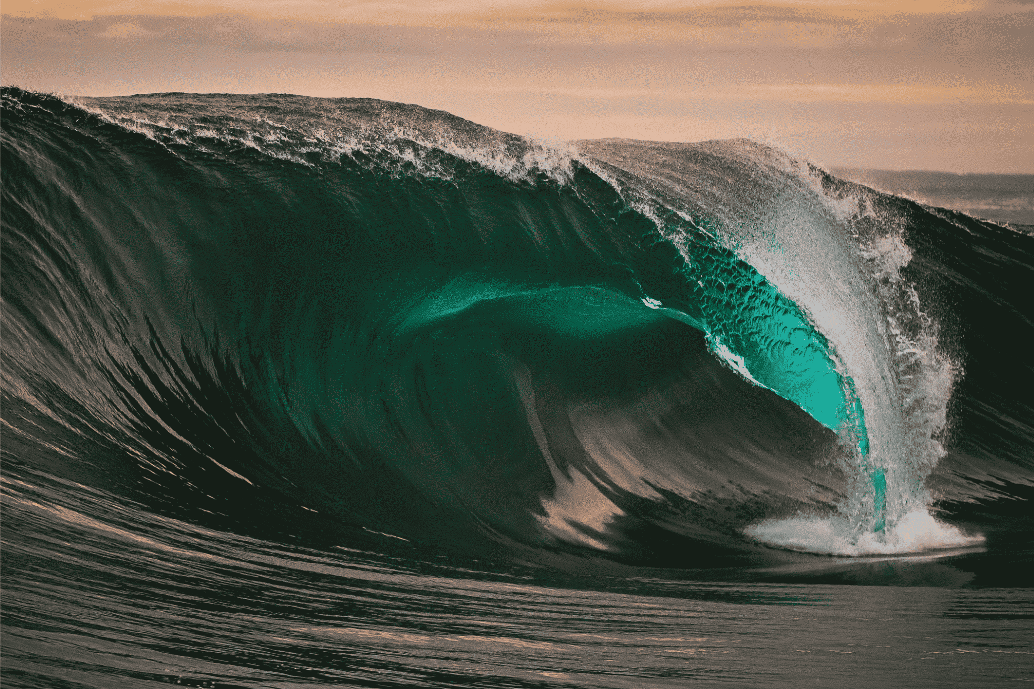 A large heavy ocean wave at its point of breaking under an evening sky, the curl already committed past the point where it can return