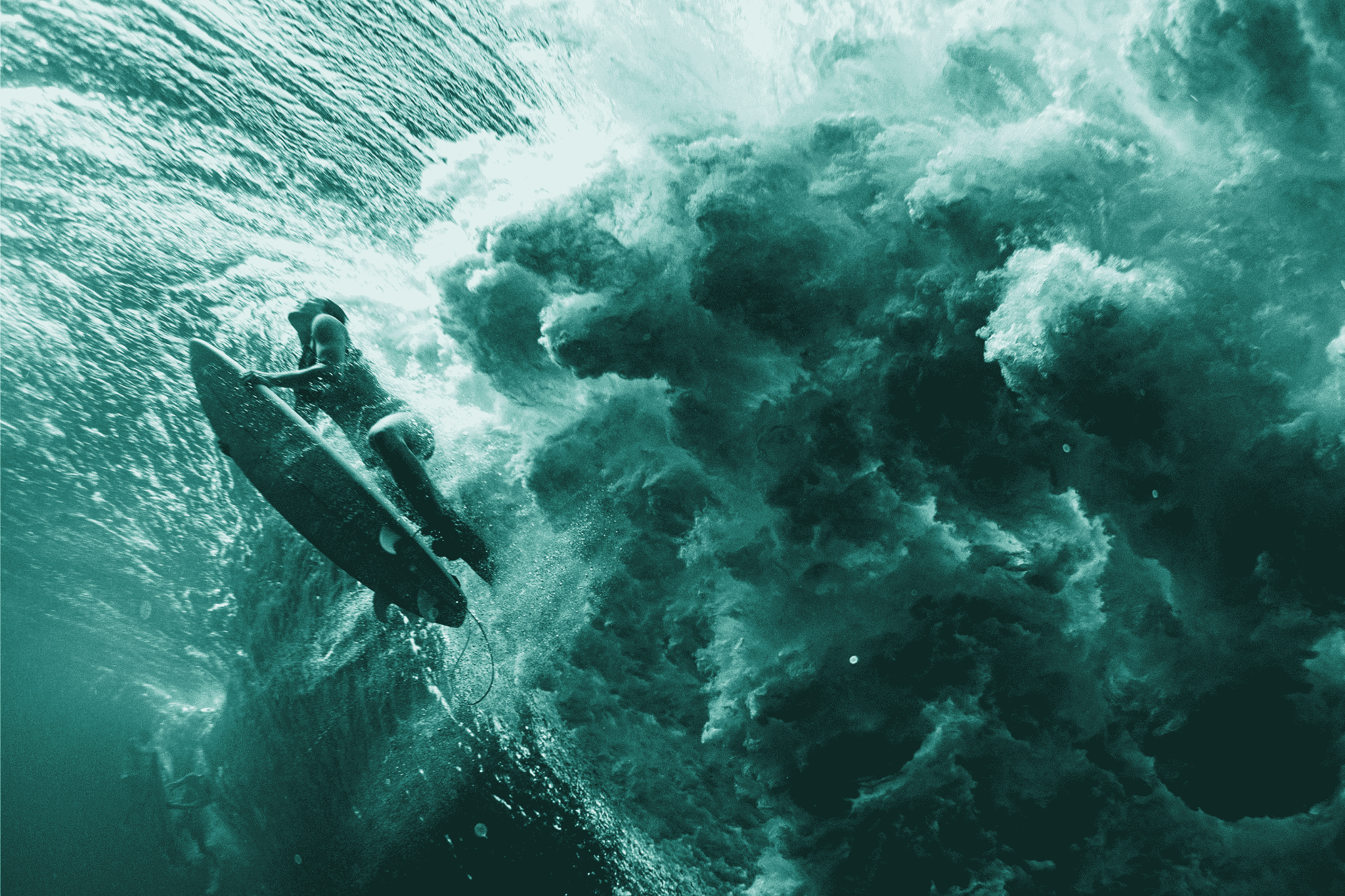Underwater view of a surfer diving beneath a powerful breaking wave, holding steady below the turbulence while the white water churns above.