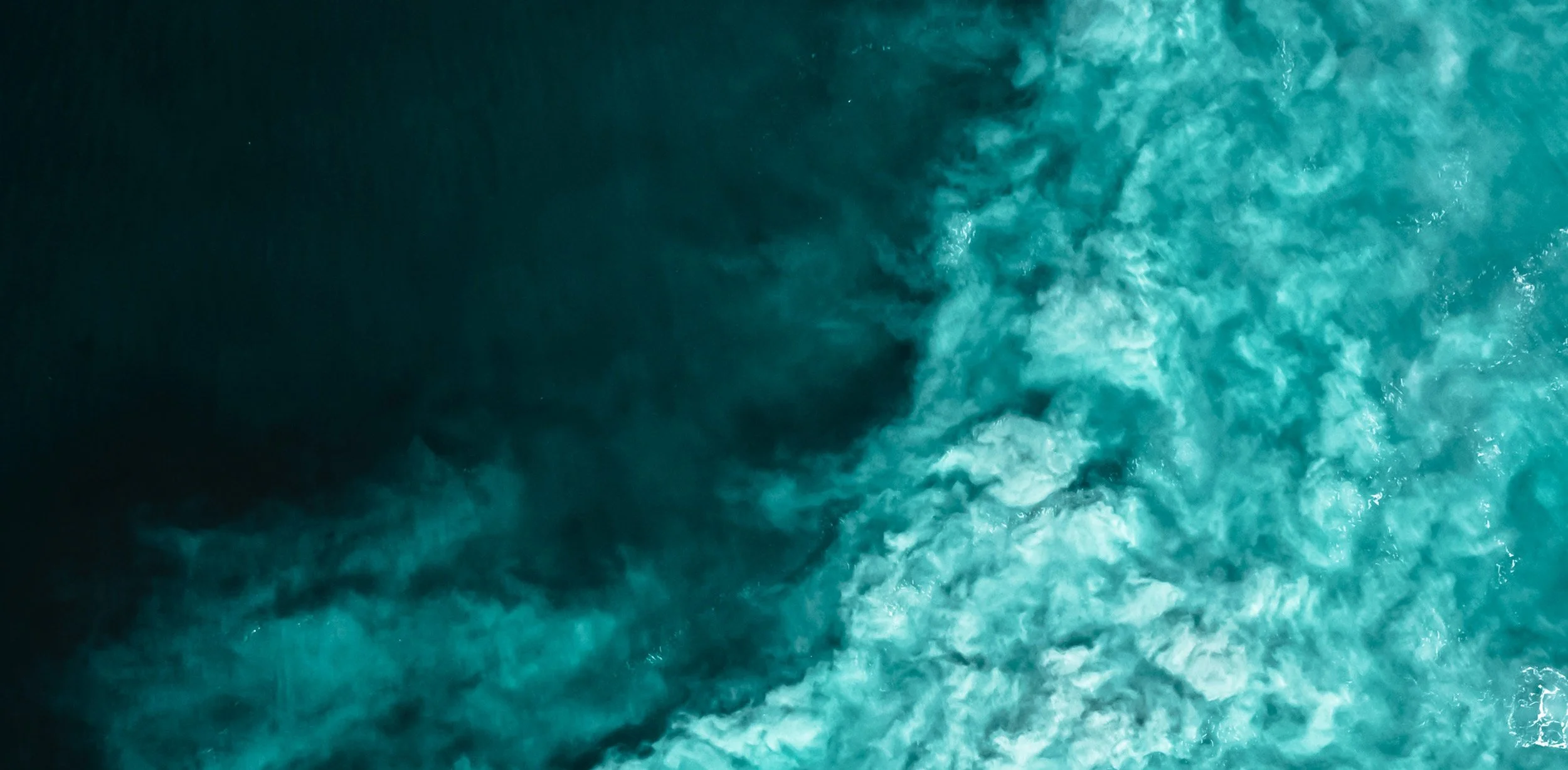 Aerial view of swirling turquoise water meeting dark sea.