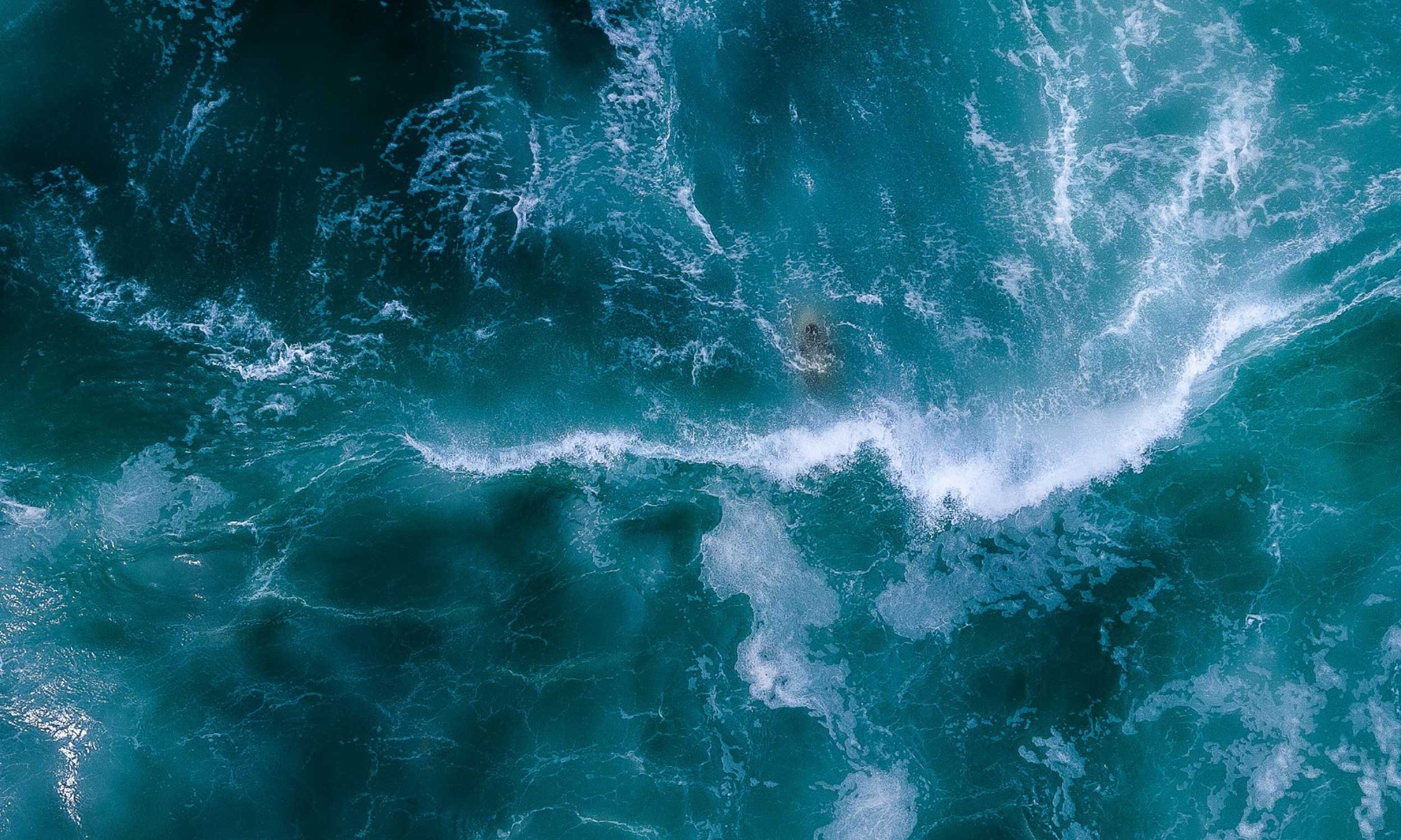 Aerial view of turquoise water with a surfer visible just beneath the surface.