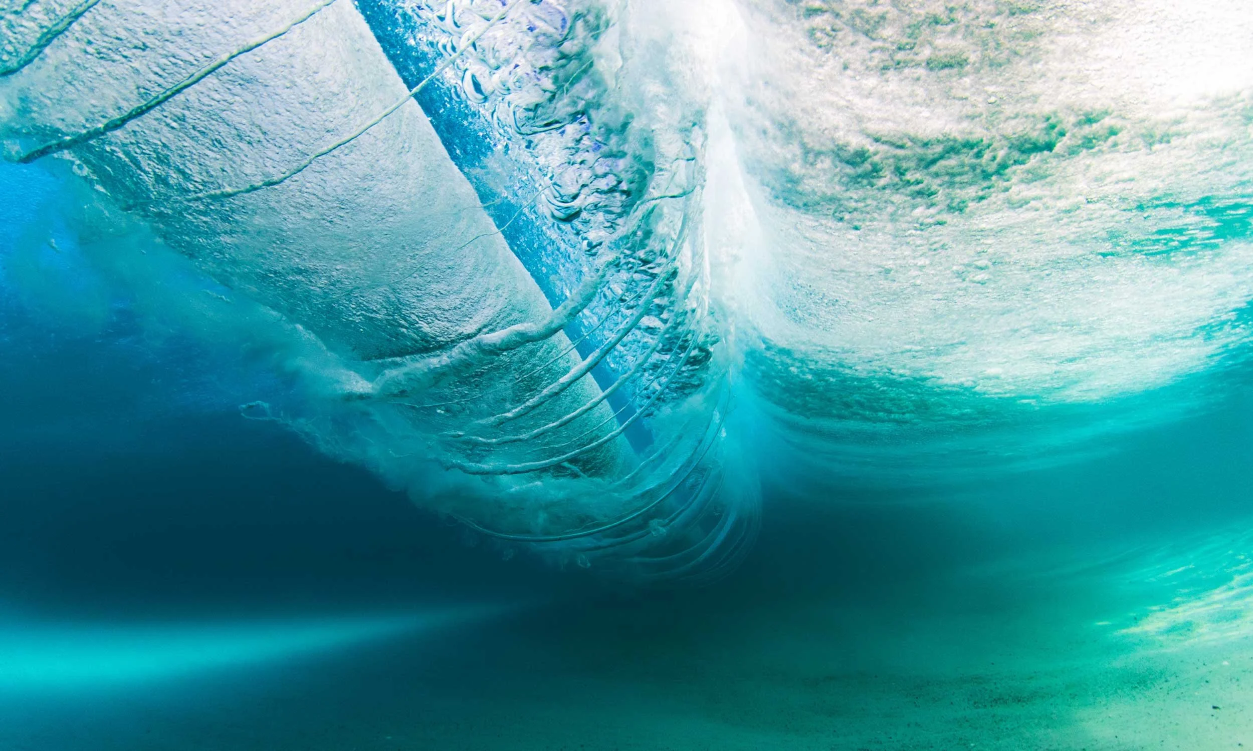 View from beneath a breaking wave, looking up through the translucent teal curl.