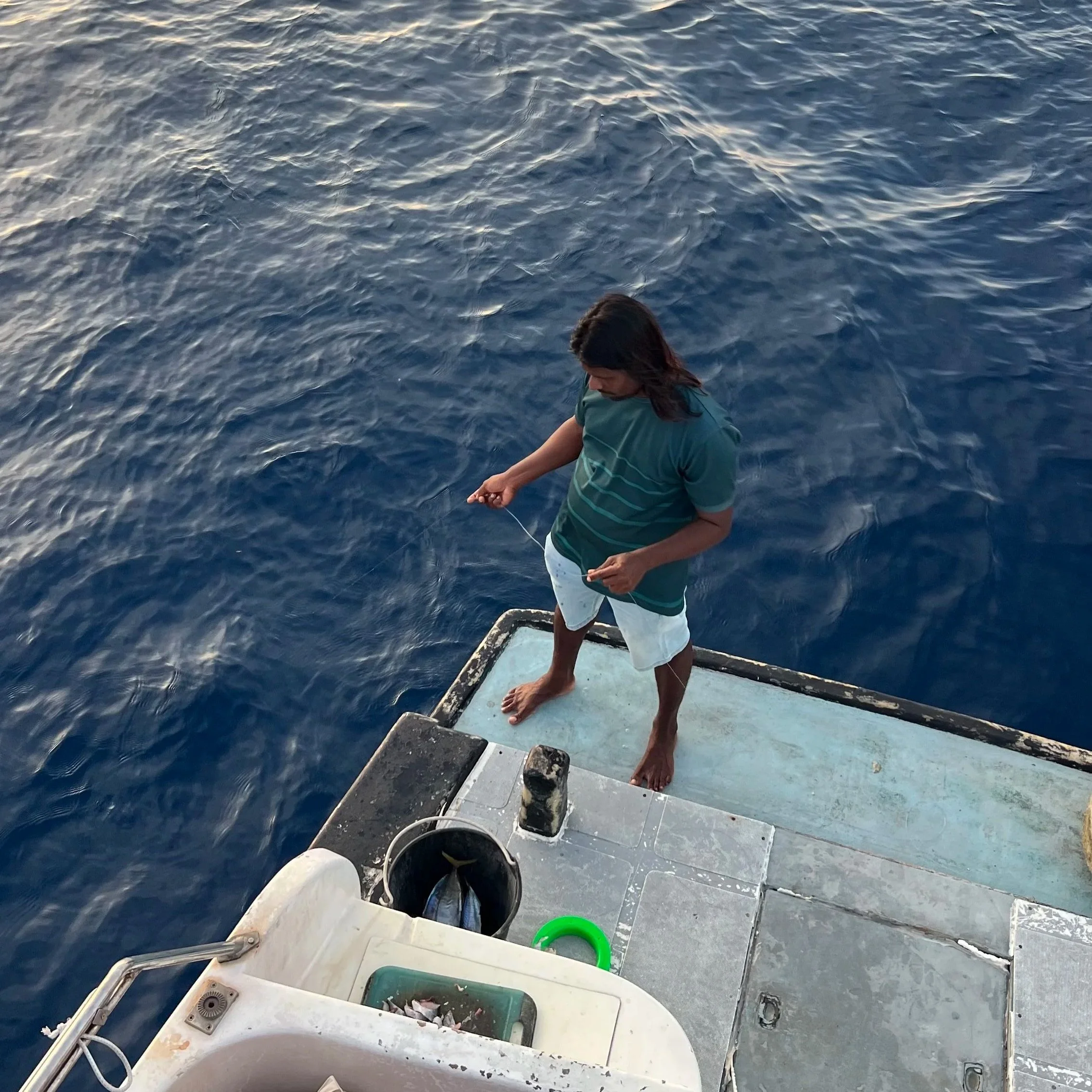 Une personne debout à la proue d'un bateau en mer, portant un t-shirt vert, regardant vers le bas, avec l'eau autour du bateau.