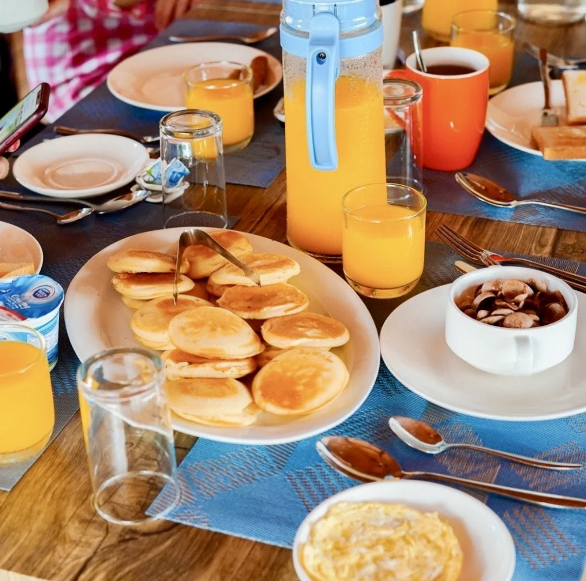 Petit déjeuner avec des pancakes, du jus d'orange, un bol d'haricots, et divers autres aliments sur une table en bois.