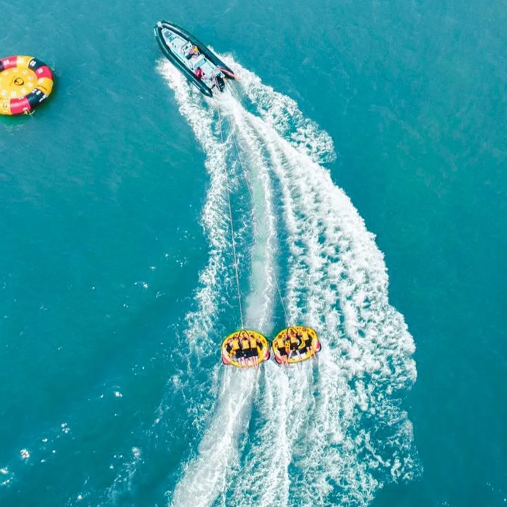 Une personne fait du wakeboard derrière un bateau dans une mer turquoise, accroché à deux bouées de sécurité jaunes et noires.