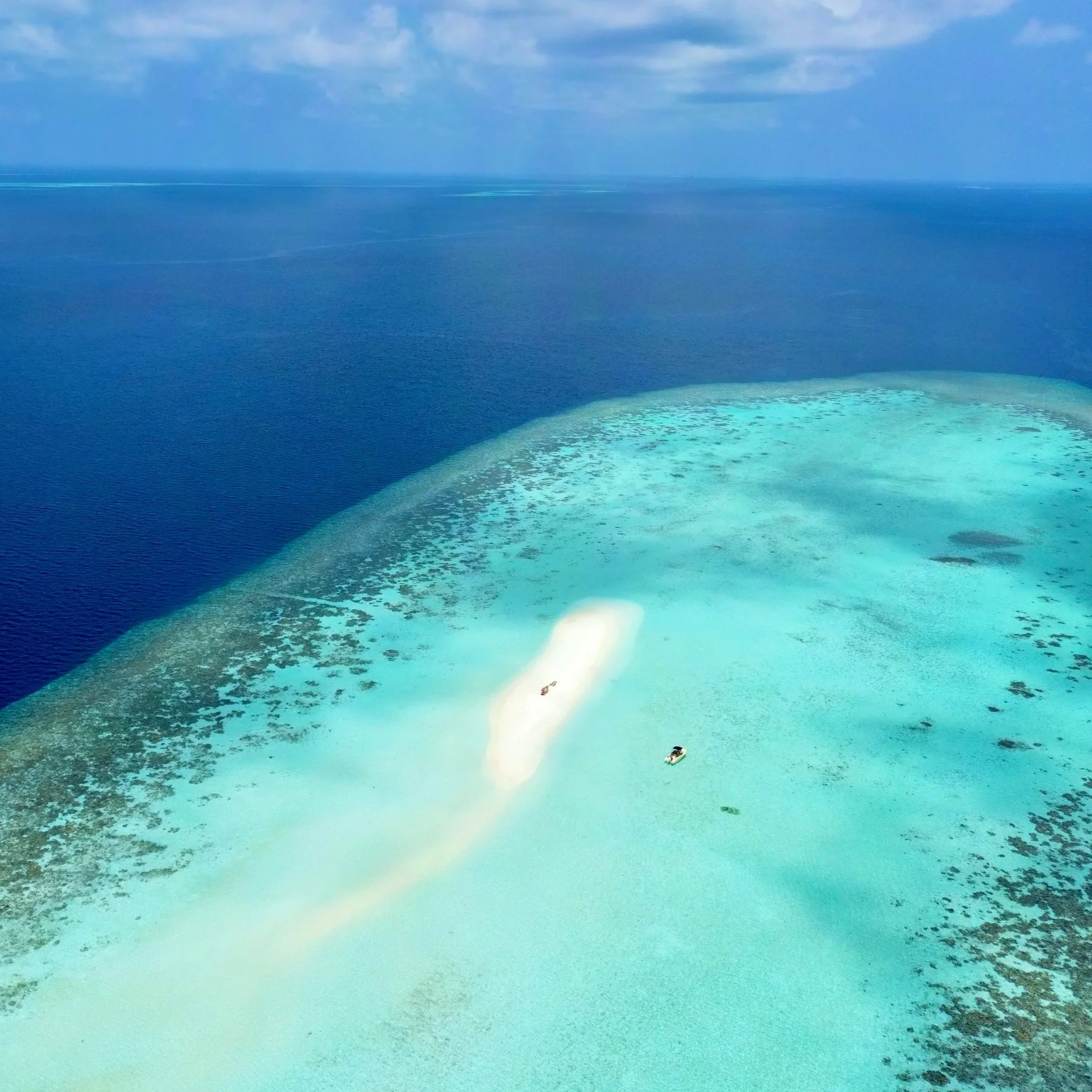 Vue aérienne d'une mer turquoise avec un récif corallien et deux bateaux.