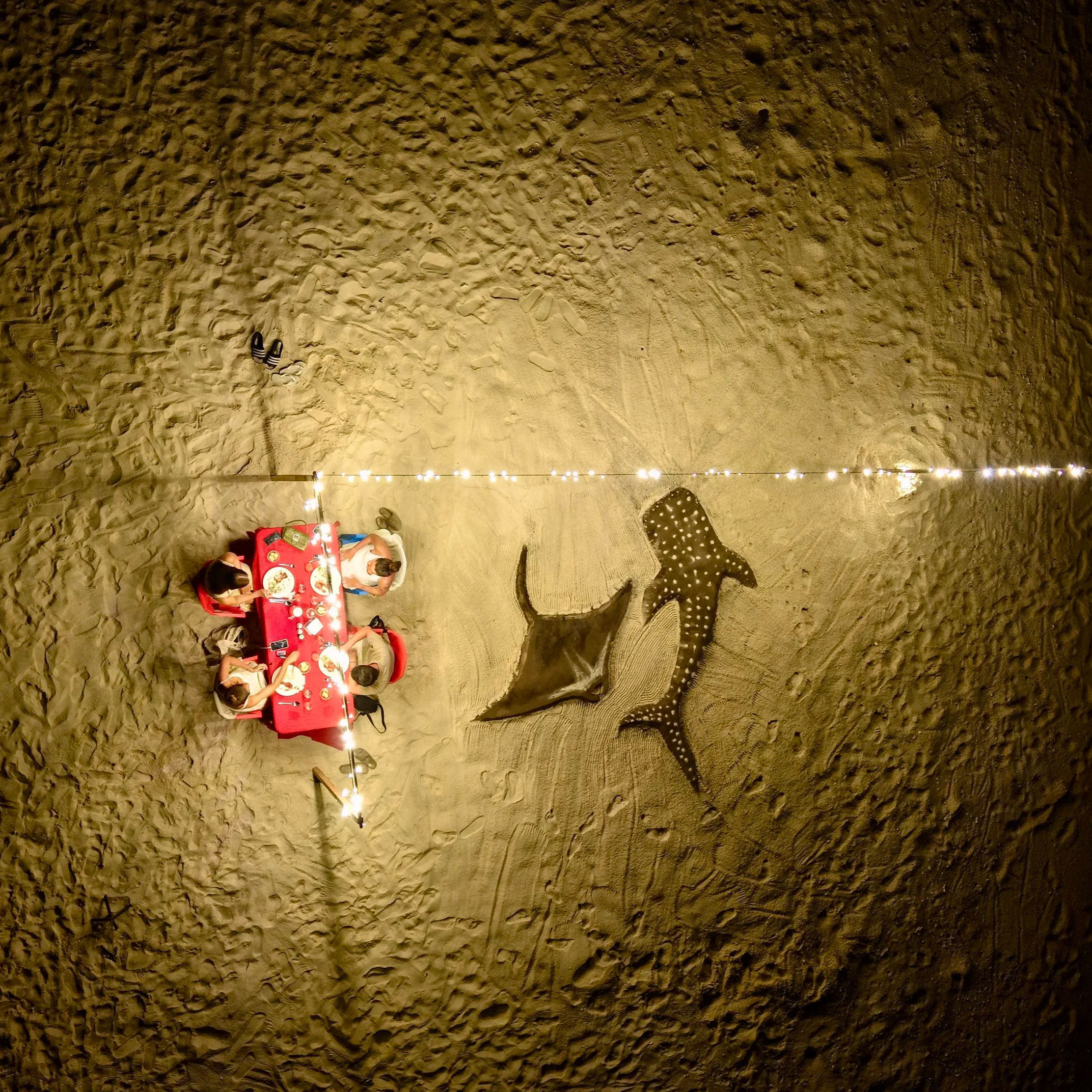 Une table rouge avec quatre enfants qui mangent, à côté d'une décoration de plage avec une grande tortue marine en polystyrène noir et blanc, et un mur en sable.