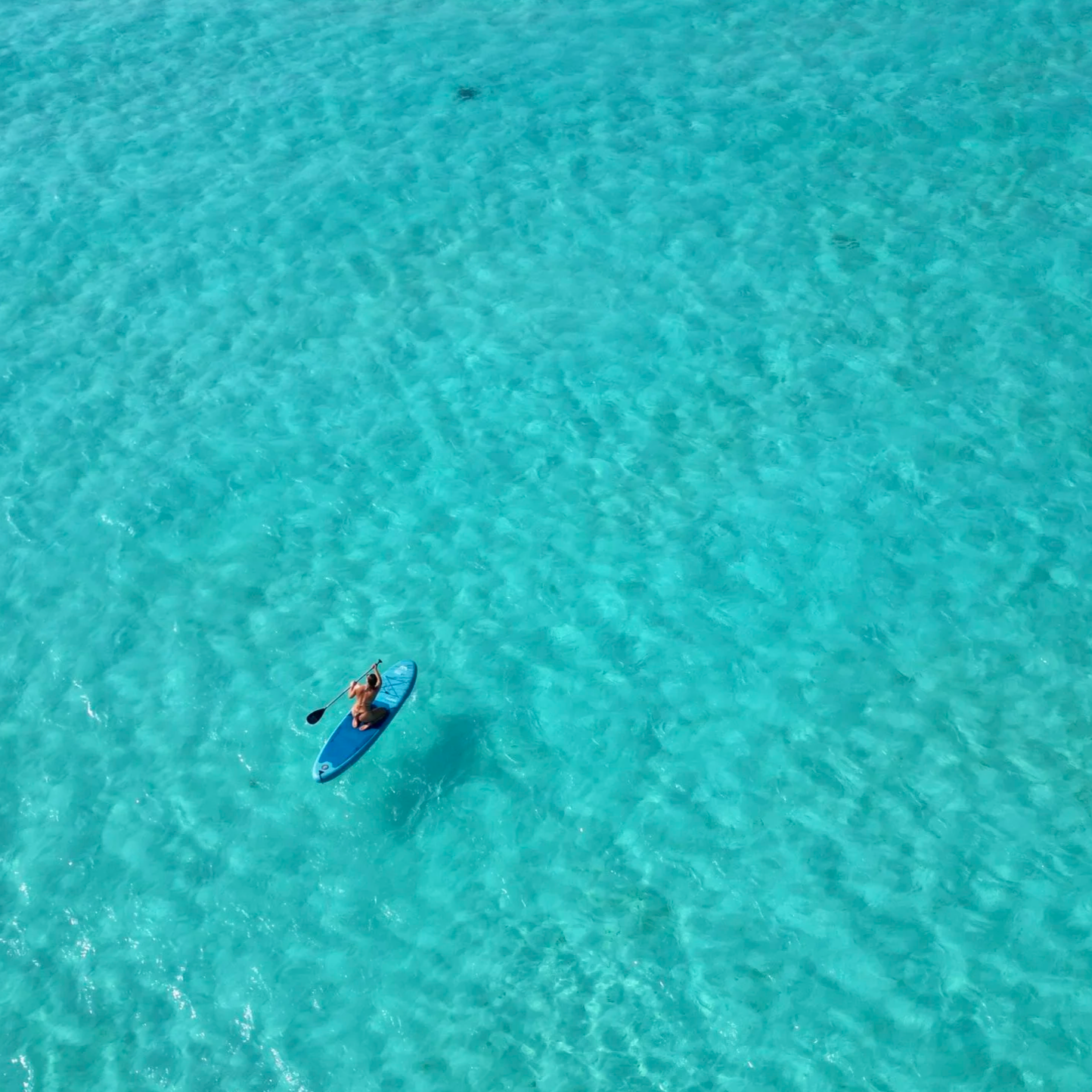 Une personne faisant du paddle dans une mer turquoise claire.