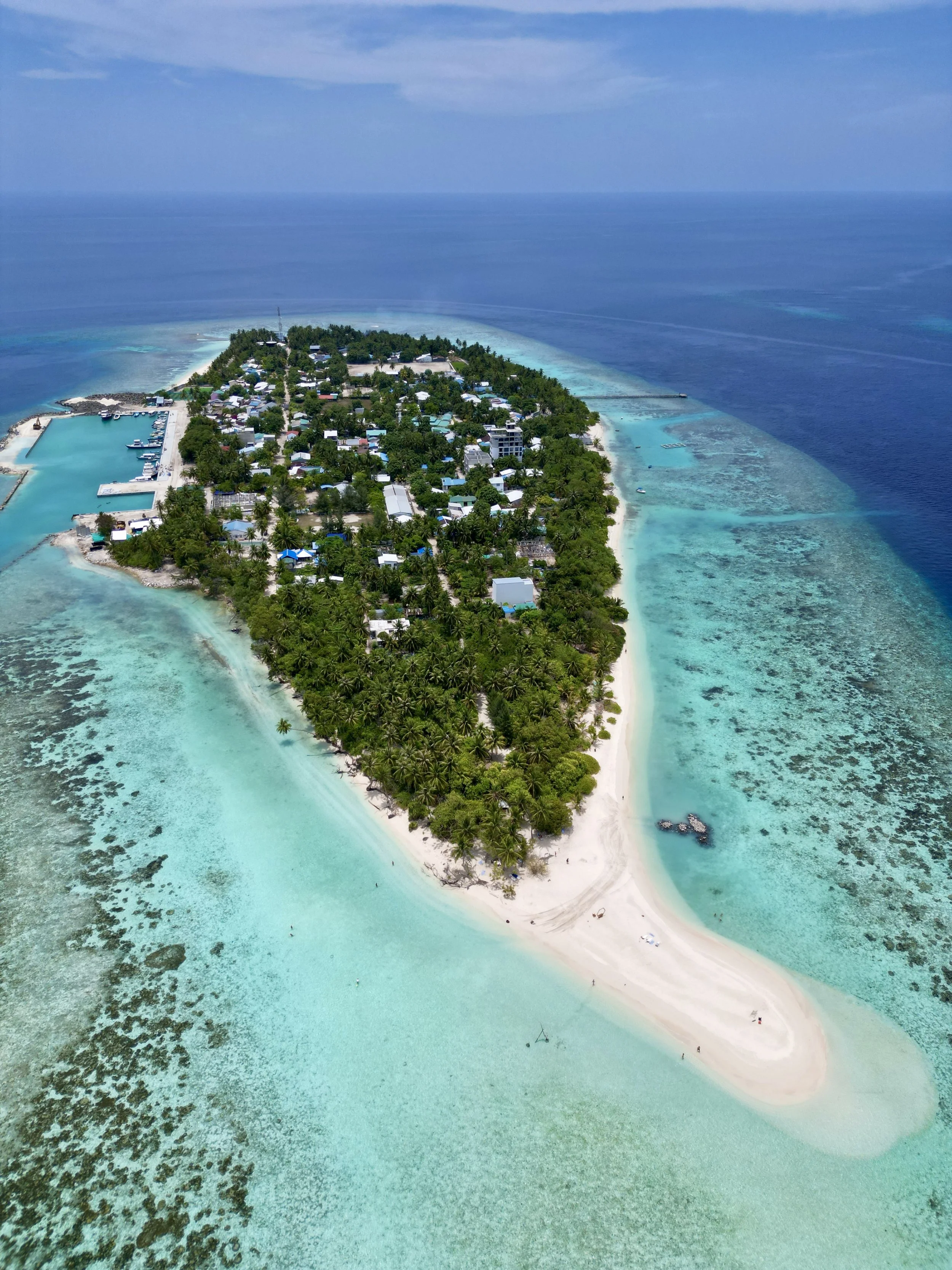 Une île tropicale avec des plages de sable blanc, des arbres verts, entourée d'une mer turquoise et d'une barrière de corail visible depuis l'air.