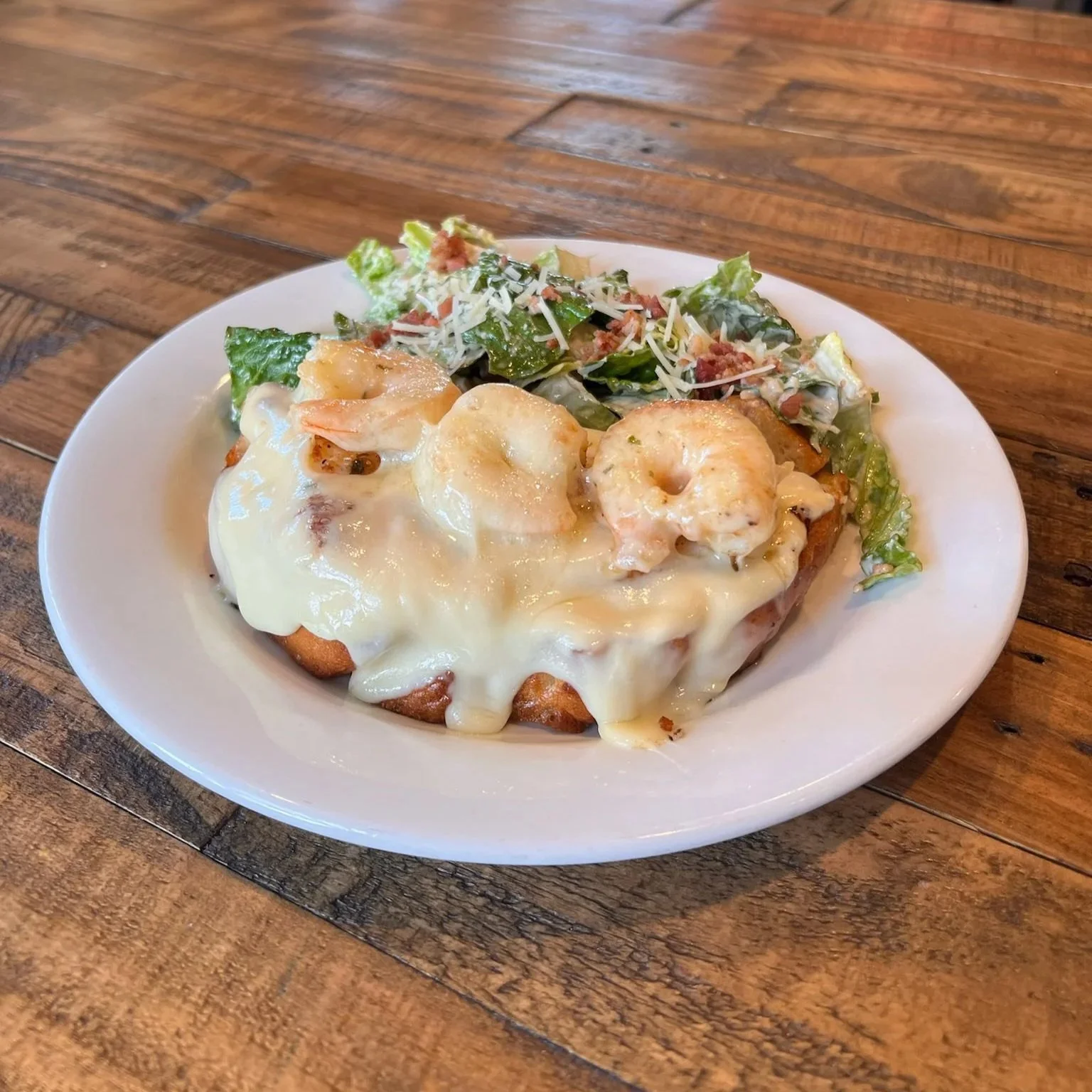 A plate of shrimp and cheese casserole with side salad on a wooden table.