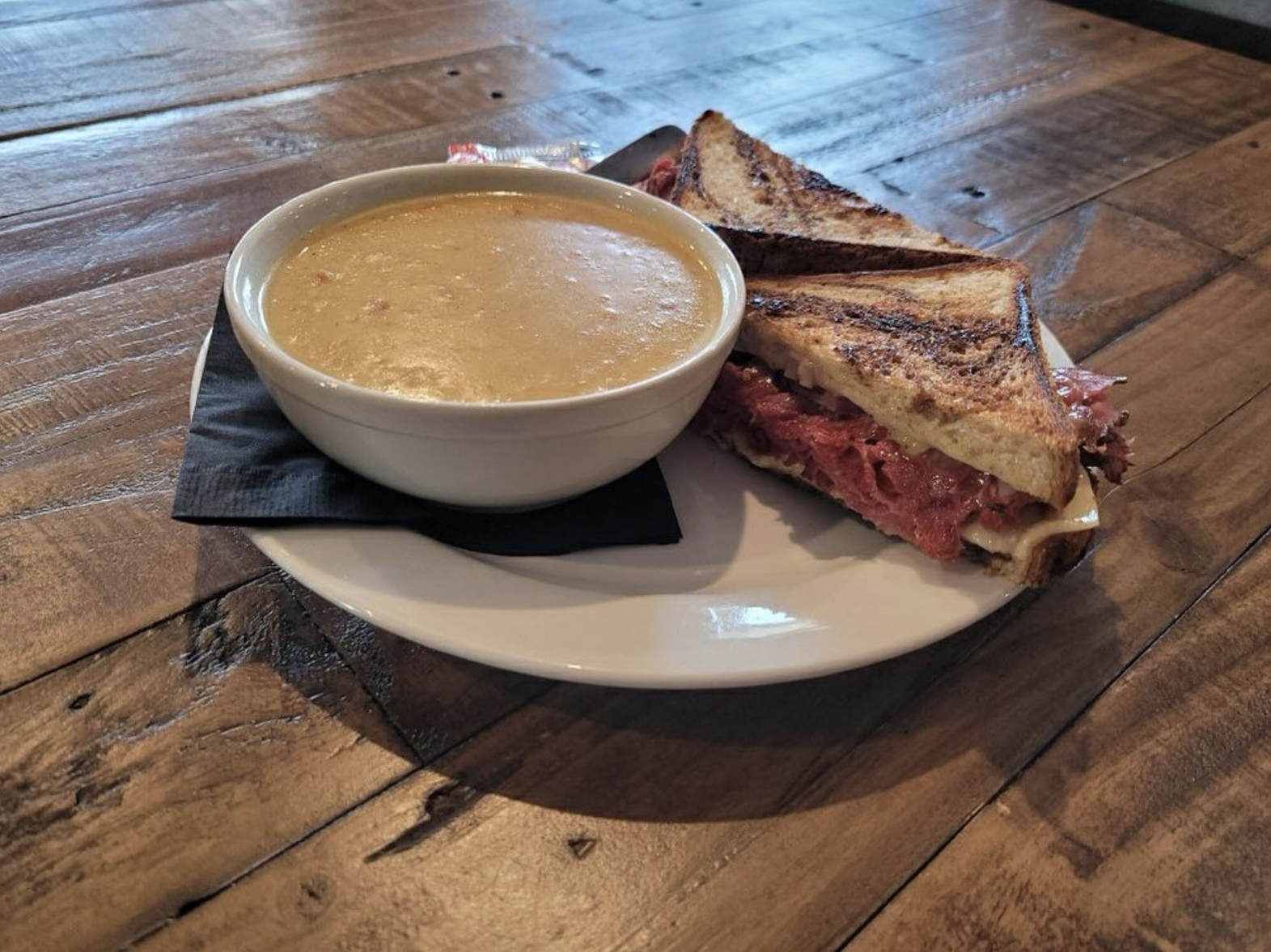 A plate with a cup of bowl of soup and a grilled sandwich on a wooden table.