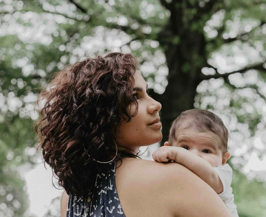 a mom holds her baby looking softly into the distance