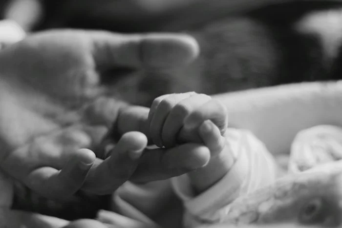 black and white image of a baby holding their mom's finger
