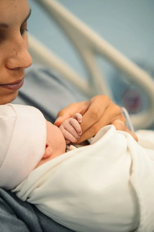 a new mom in the hospital holding her baby's hand