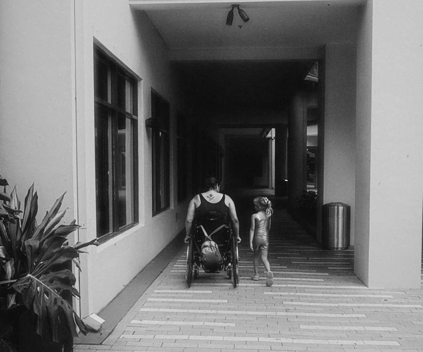 black and white film photo of a mom in a wheelchair with her young daughter walking next to her