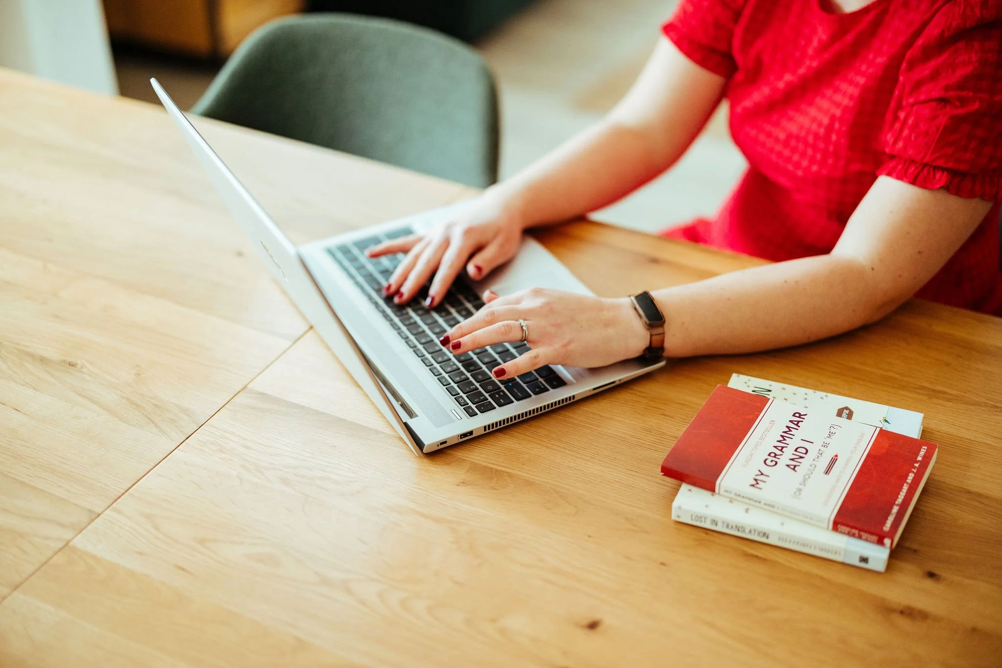 A person wearing a red dress working on a laptop at a wooden table with books on social justice and racial inequality nearby.