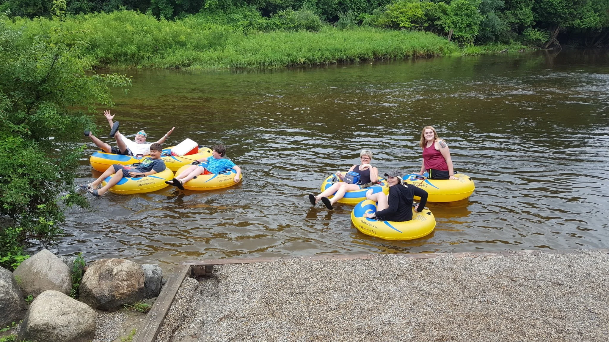 A group of people floating on rented tubes in a river surrounded by green trees and foliage.
