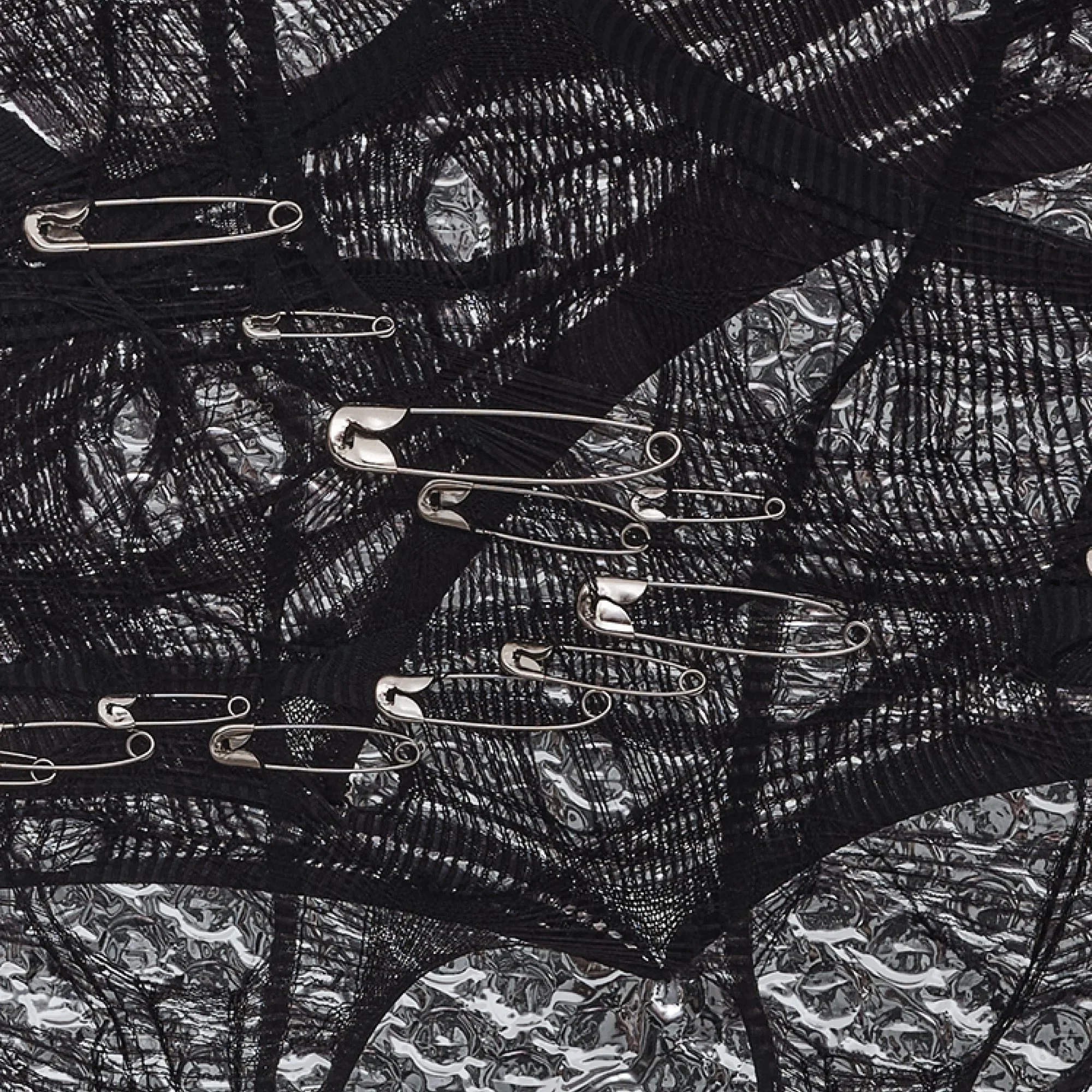 Detail of "Silver Dreams: Act 3 - Heart" by Nicole Bajger; reflective silver industrial packaging visible through black textile.