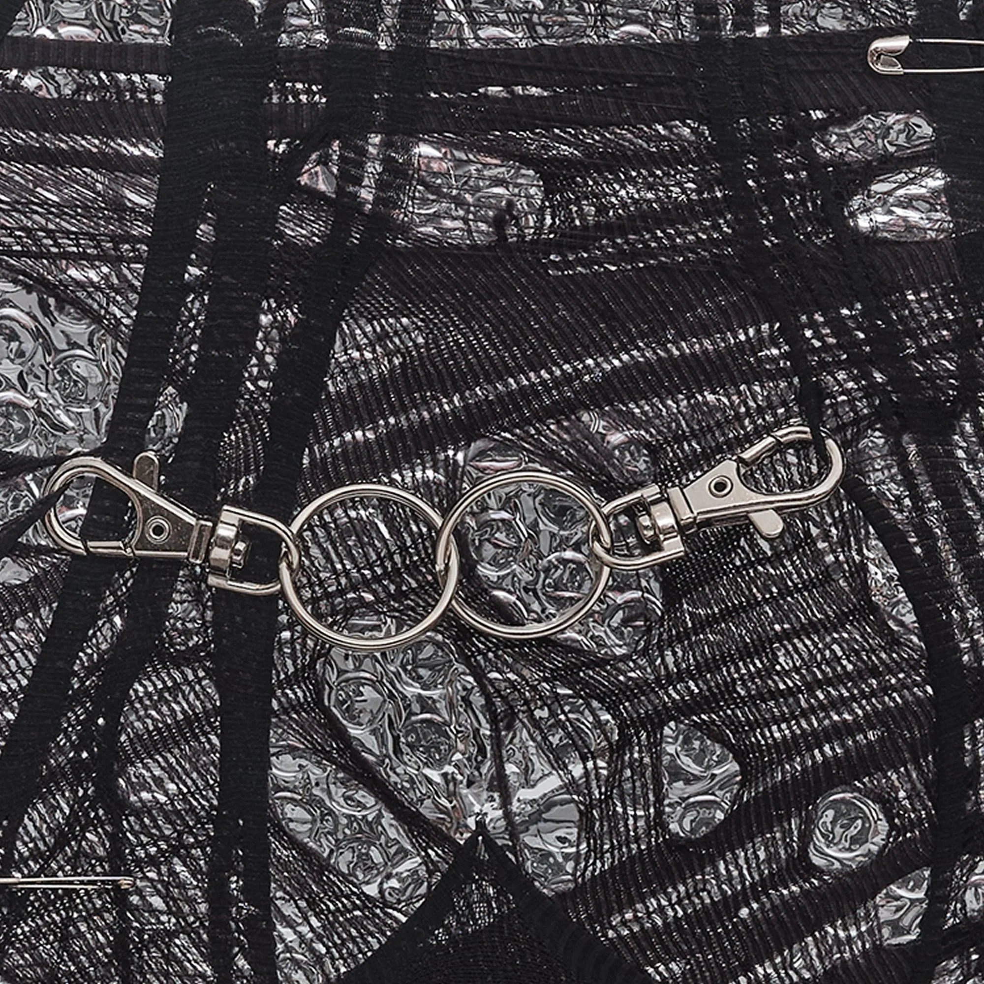 A close-up of a black fabric with silver safety pins attached and decorative black tulle overlay.