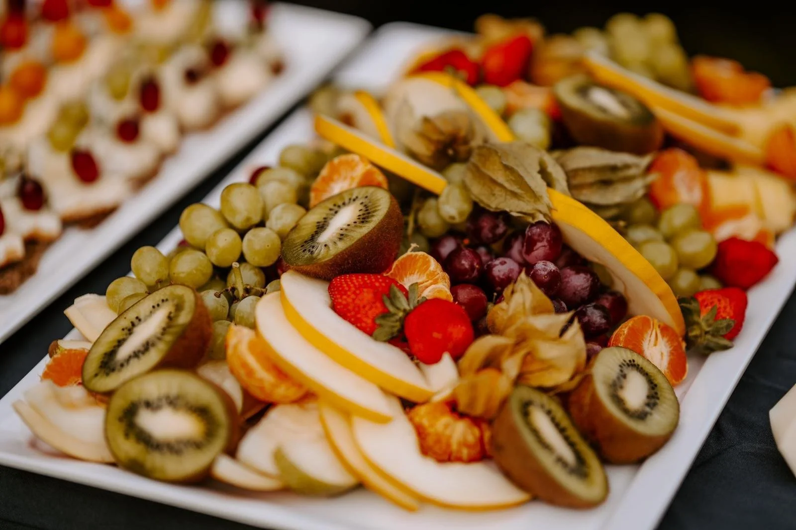 Bunte Obstplatte mit Kiwi, Trauben, Erdbeeren, Mandarinen, physalis, Zitronenscheiben und Wassermelone.
