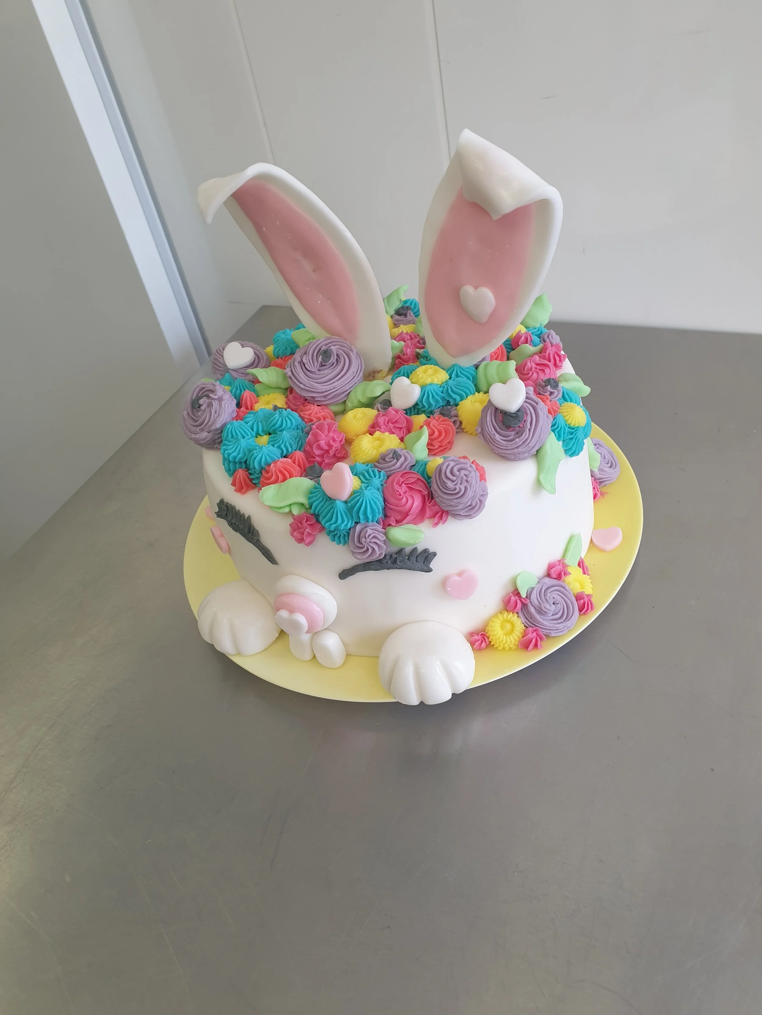 Eine bunte Geburtstagstorte mit Mausrustern, bunten Buttercremeblasen und großen weißen Schokoladen-Maushintern, die wie Ohren aussehen.
