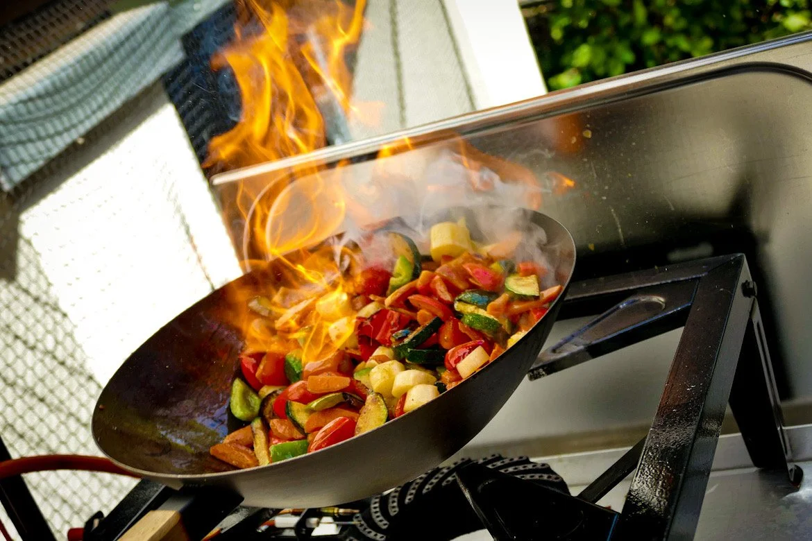 Gemüse wird beim Braten in der Pfanne angezündet, Flammen schlagen hoch.