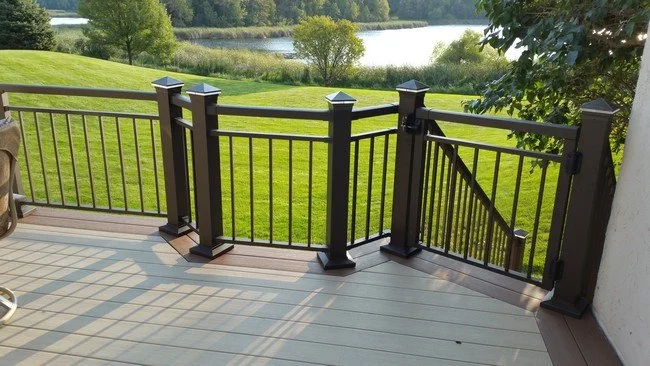 View of a deck with black metal railing and gate, overlooking a grassy yard, trees, and a river in the background.