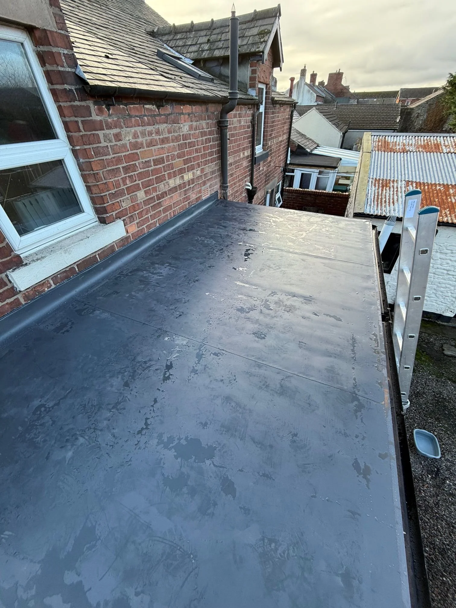 The same roof after a full restoration, now featuring a clean, seamless grey membrane and professional edge trims.