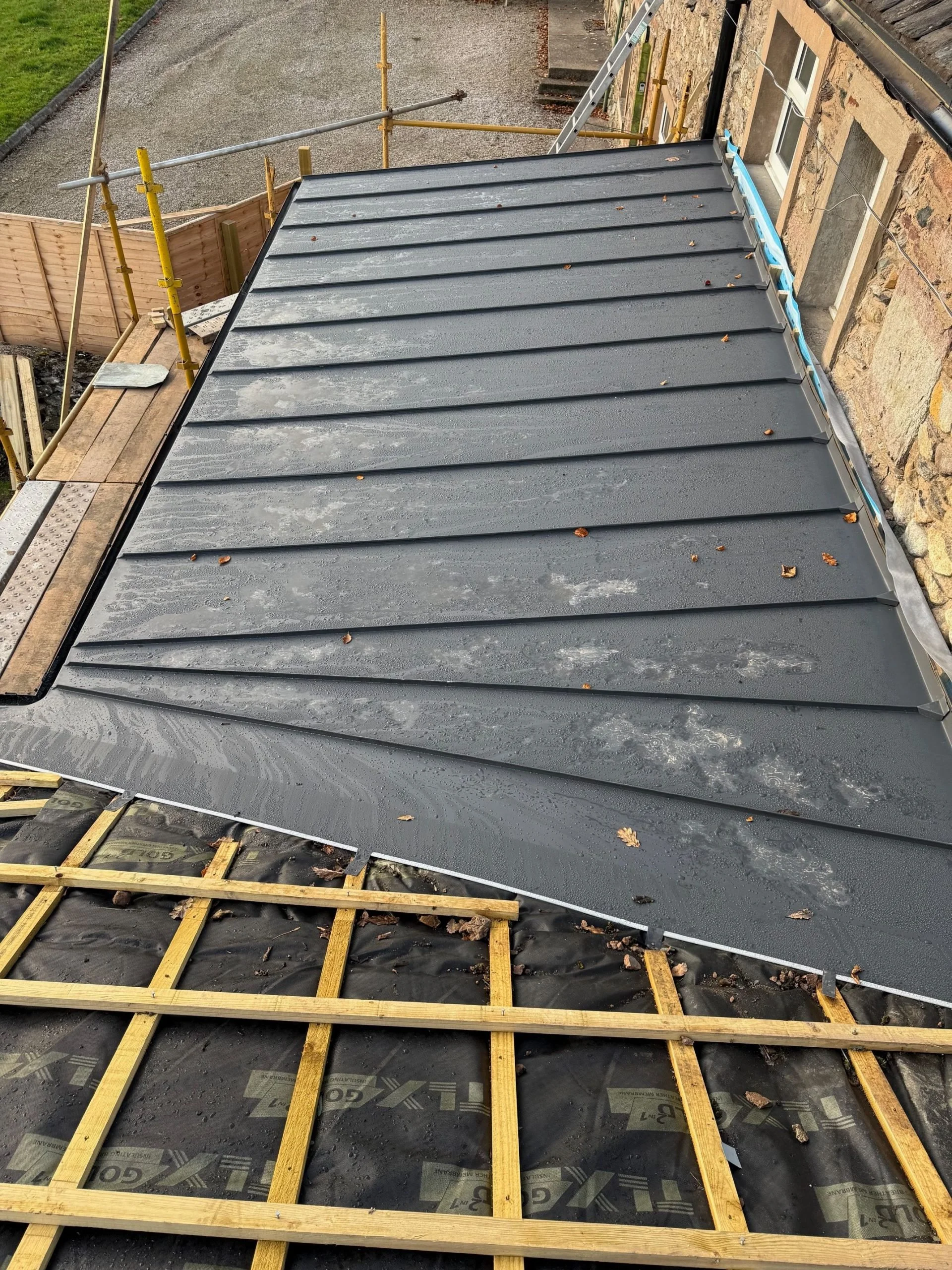 Behind the scenes detailing of custom-cut, tapered metal roofing panels laid precisely over structural timber battens before final seam locking.