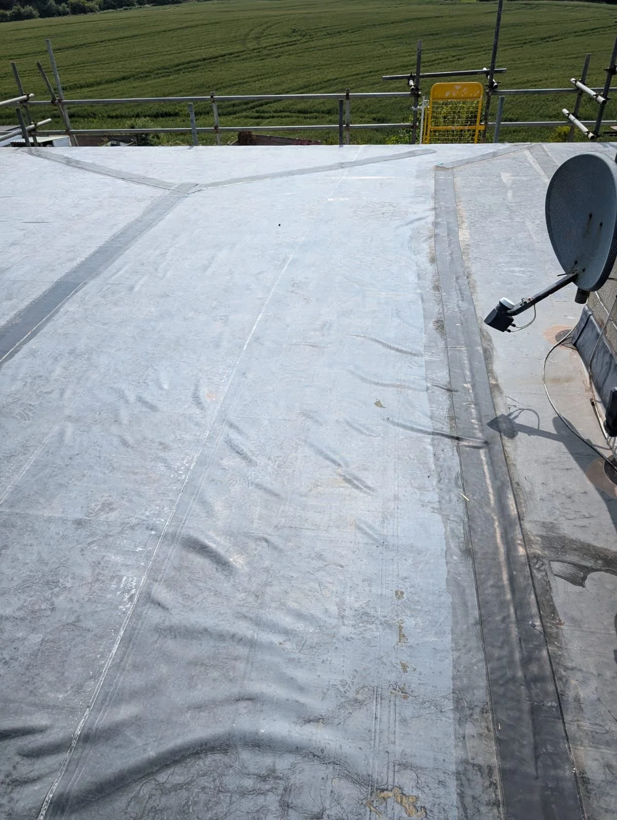 Close-up of cracking perimeter tapes and separating seams on a flat roof installation, showing why standard glue fails over time.